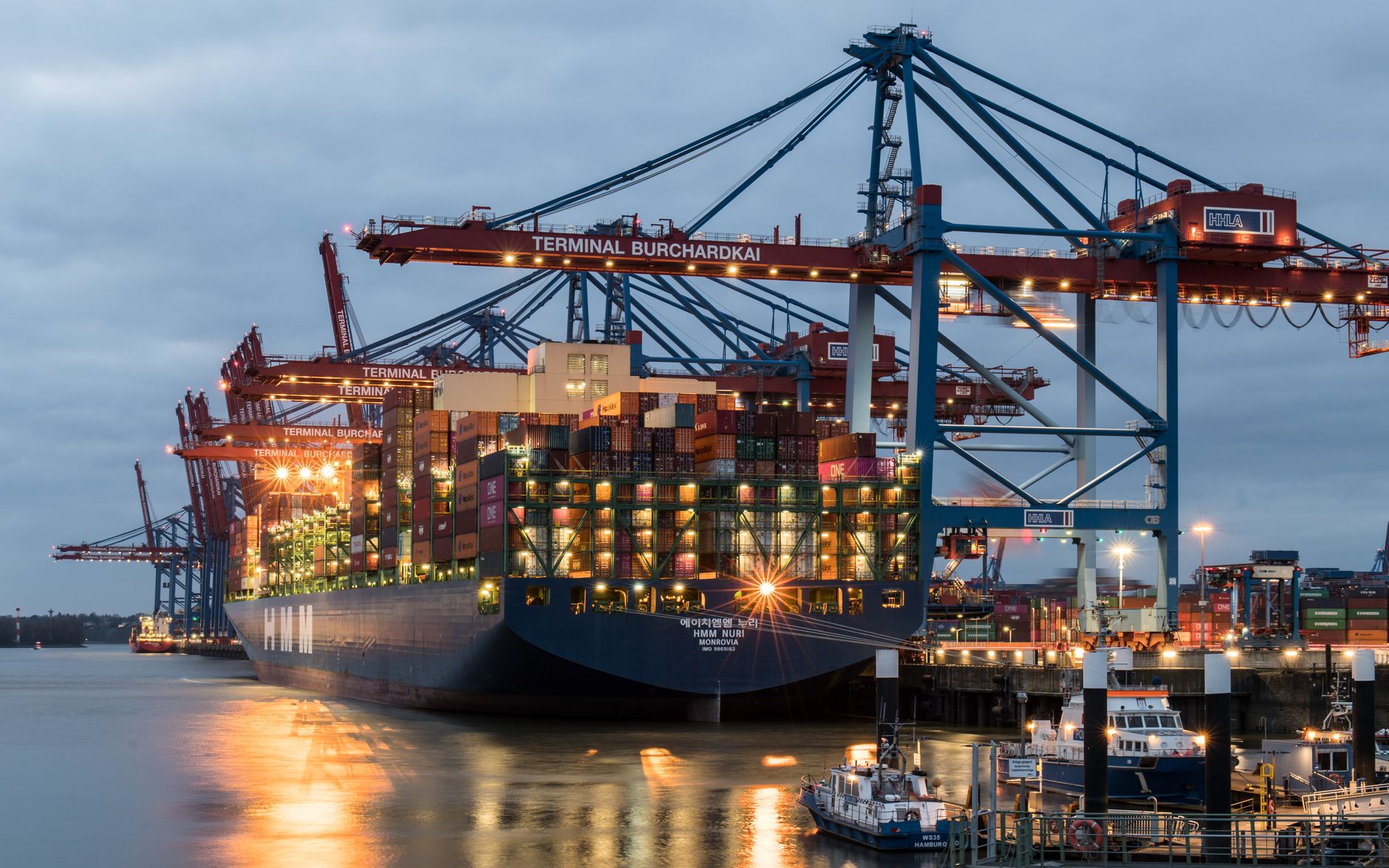 Shipping containers stacked at a freight terminal illustrate the landed-cost pressures affecting equipment orders.
