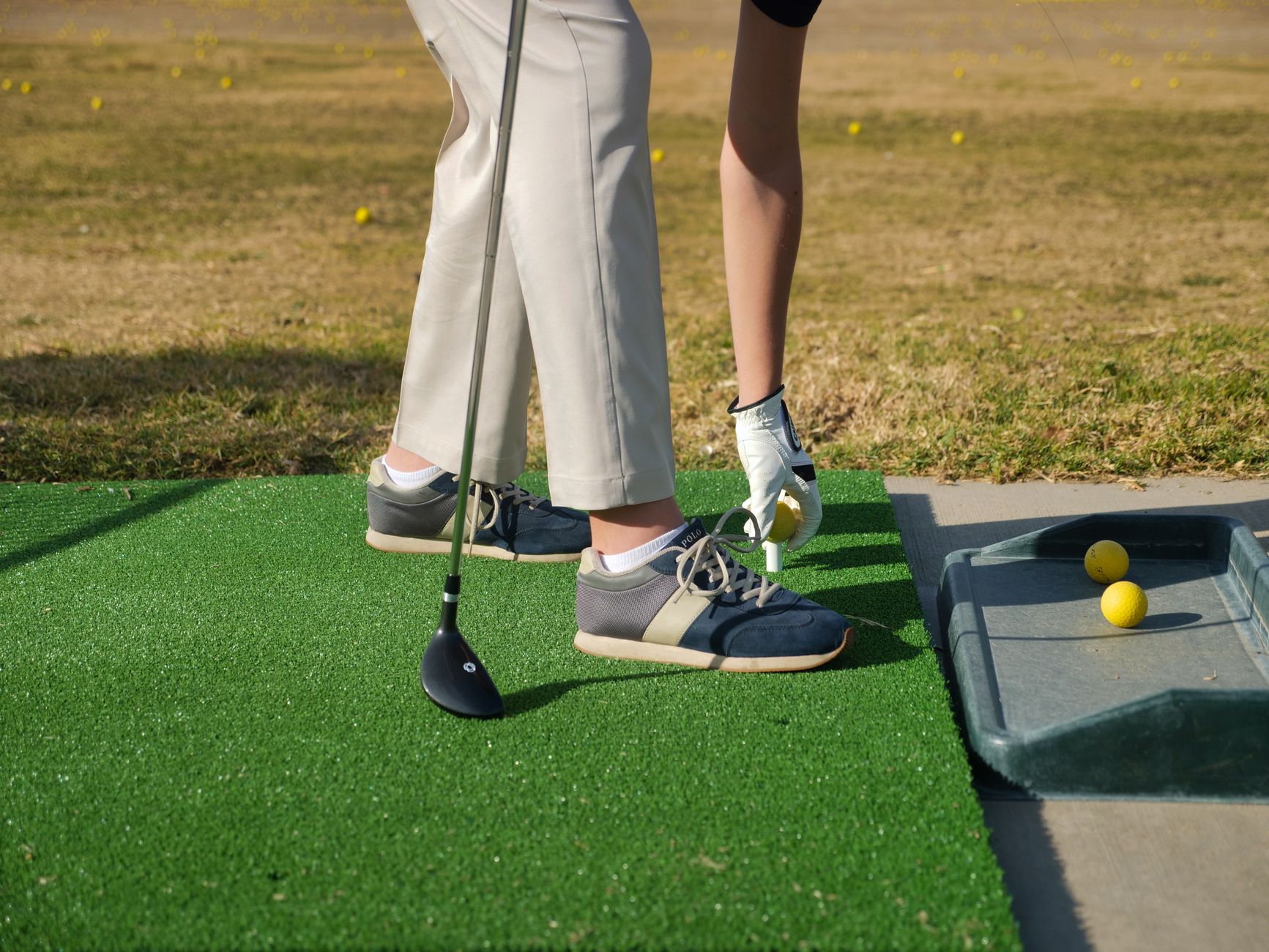 A golfer practices from a bay overlooking a busy driving range covered with golf balls.