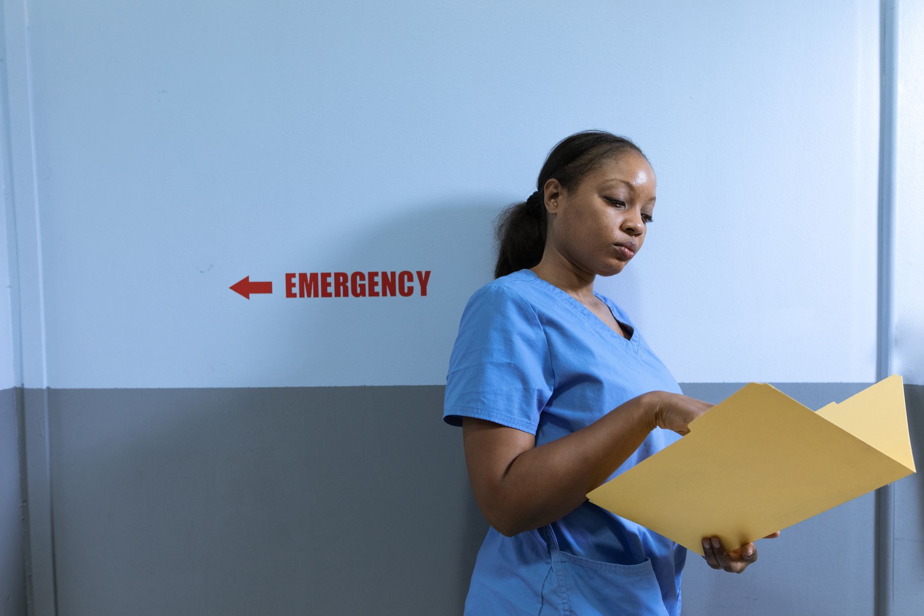 Busy hospital emergency department corridor where staff move between patient bays and central hallways.