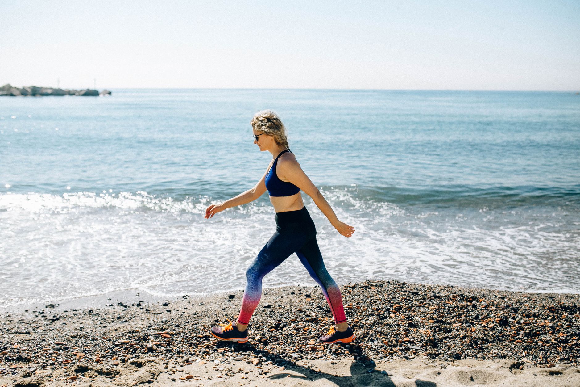 A physical therapist supports an adult patient practicing walking in an inpatient rehabilitation gym.