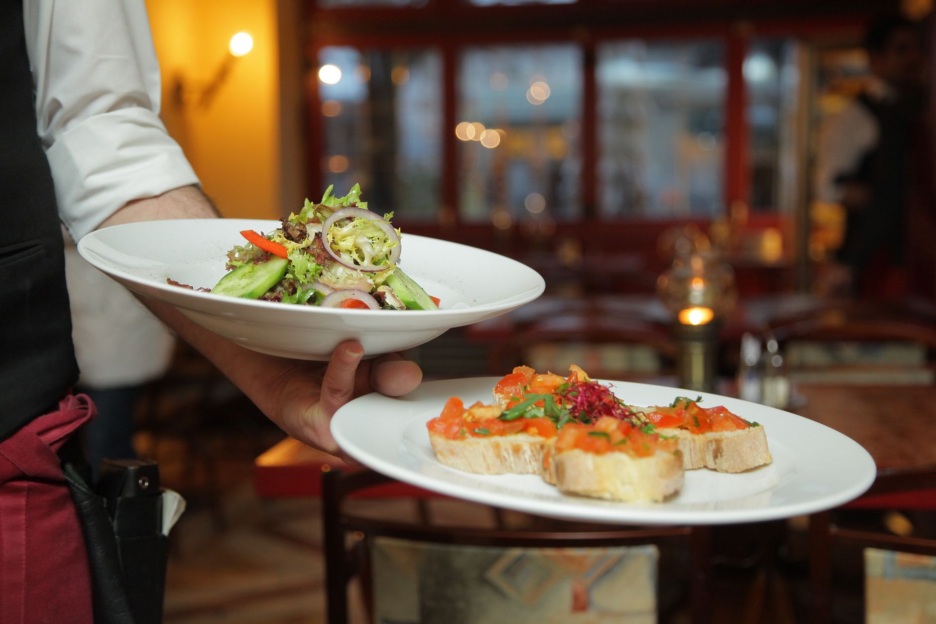 A restaurant server carrying multiple plates through a busy dining room, reflecting the repetitive front-of-house transport work this rollout was designed to support.