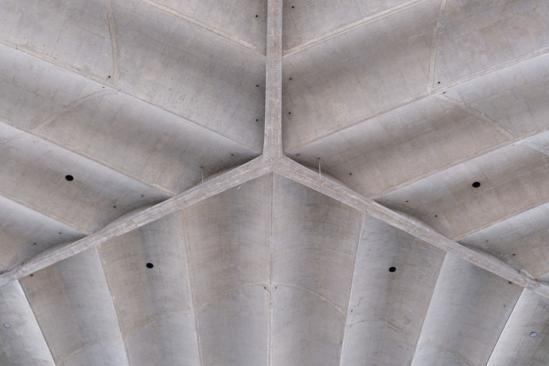 An unfinished concrete slab ceiling where MEP trades drill overhead hanger holes during a commercial build.
