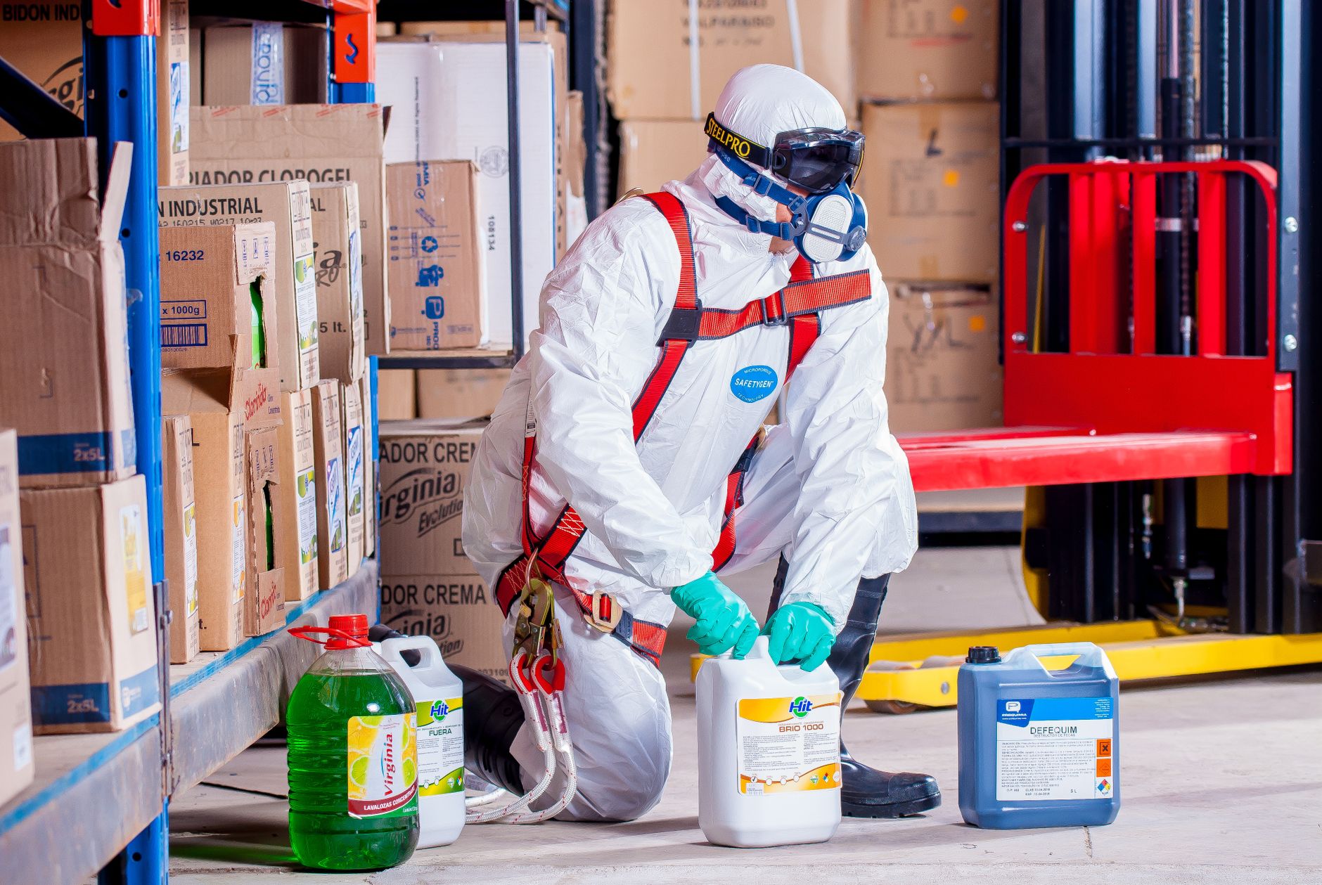 Workers handle sealed chemical-product containers in a busy factory warehouse.