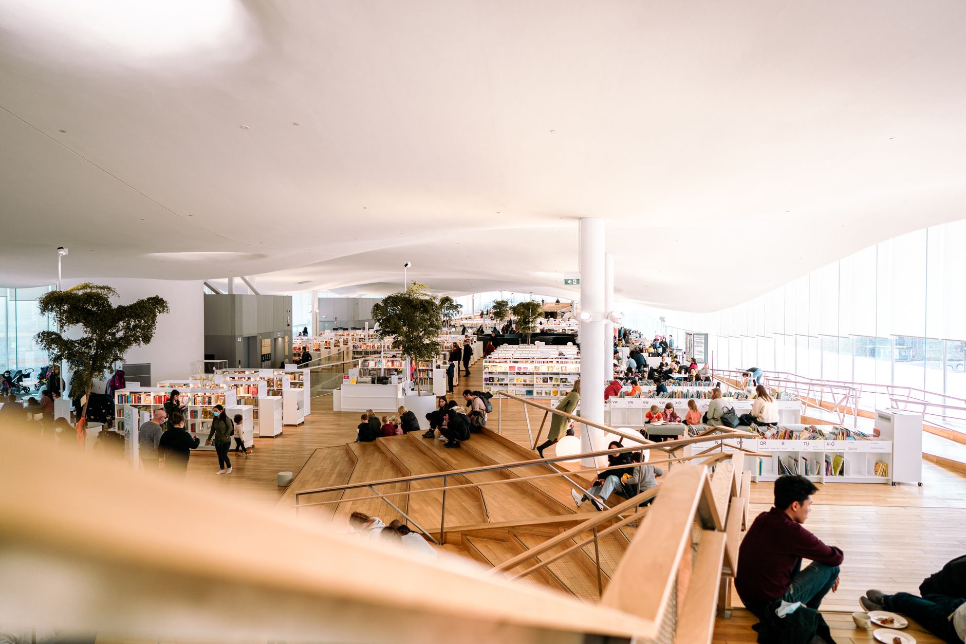Wide view of a busy modern public library interior that conveys a large, high-traffic civic reading space.