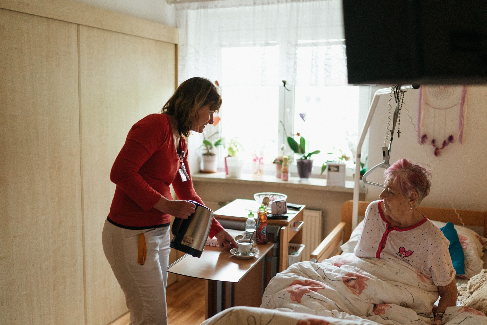 A caregiver places a plated meal in front of a seated older adult at a dining table.