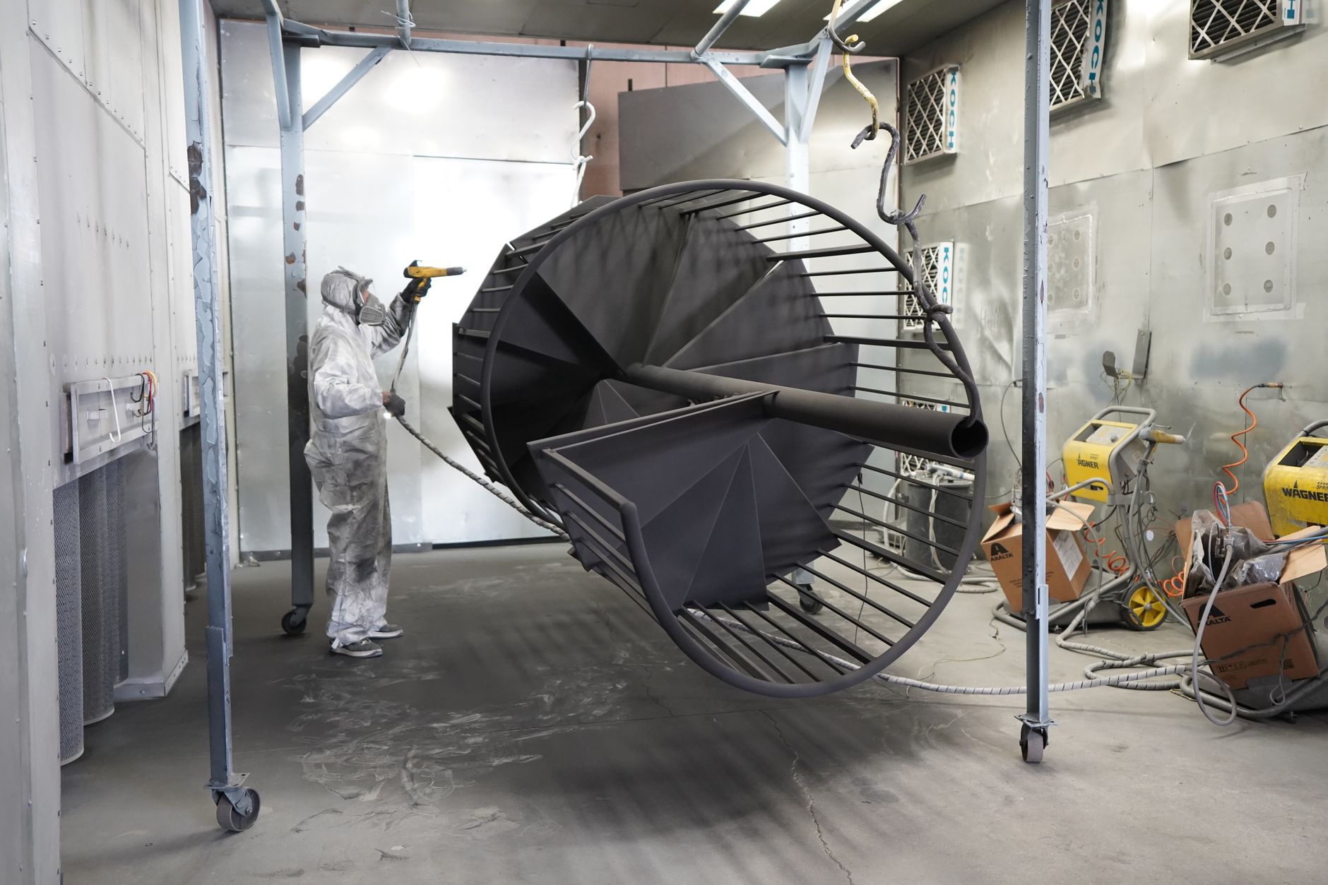 A skilled painter applies a finish inside an industrial paint booth.