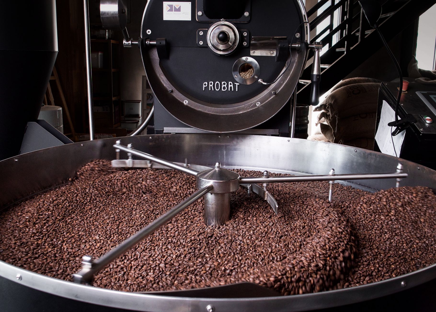 Interior of a coffee roasting and packaging facility with stainless equipment and stacked supplies.