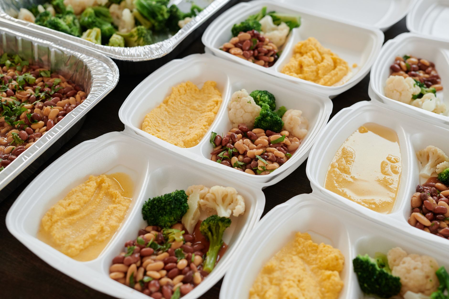 Workers assemble prepared foods into meal trays along an existing commercial kitchen line.