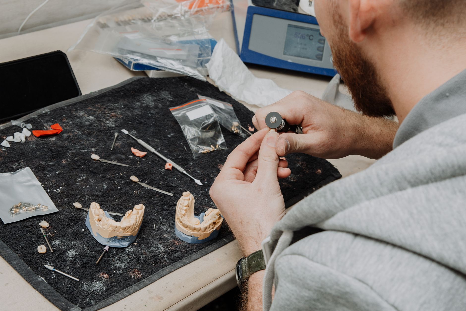 A dental laboratory technician carefully examines a crown at a brightly lit workbench.