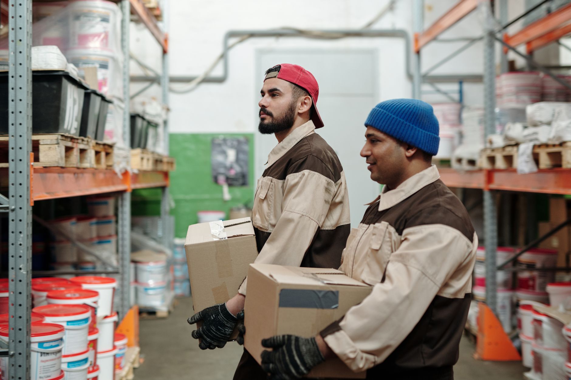 An employee carries a box across a warehouse floor toward a pallet.