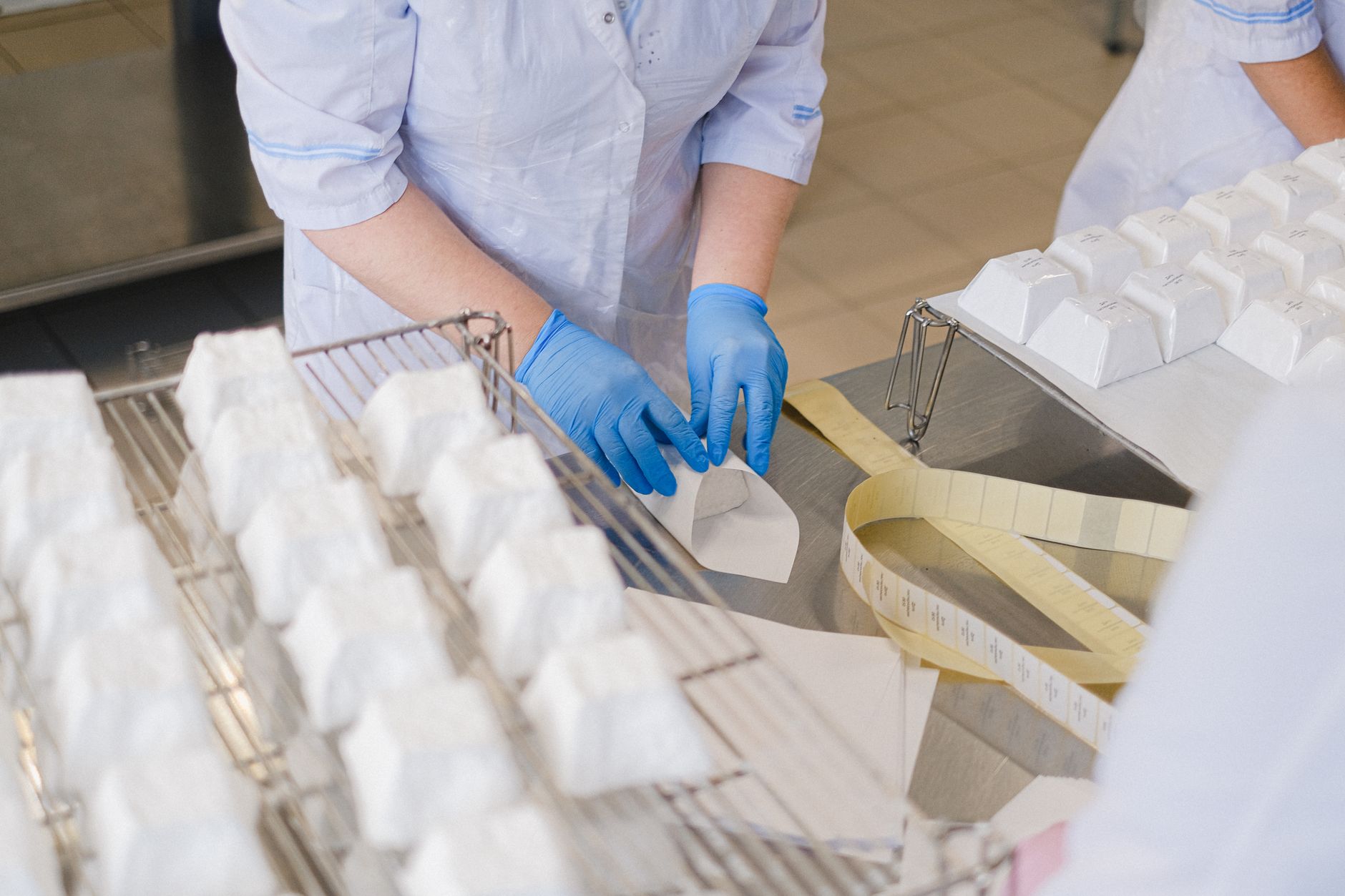 Factory operators pack finished goods at a workstation beside stacked shipping cartons.