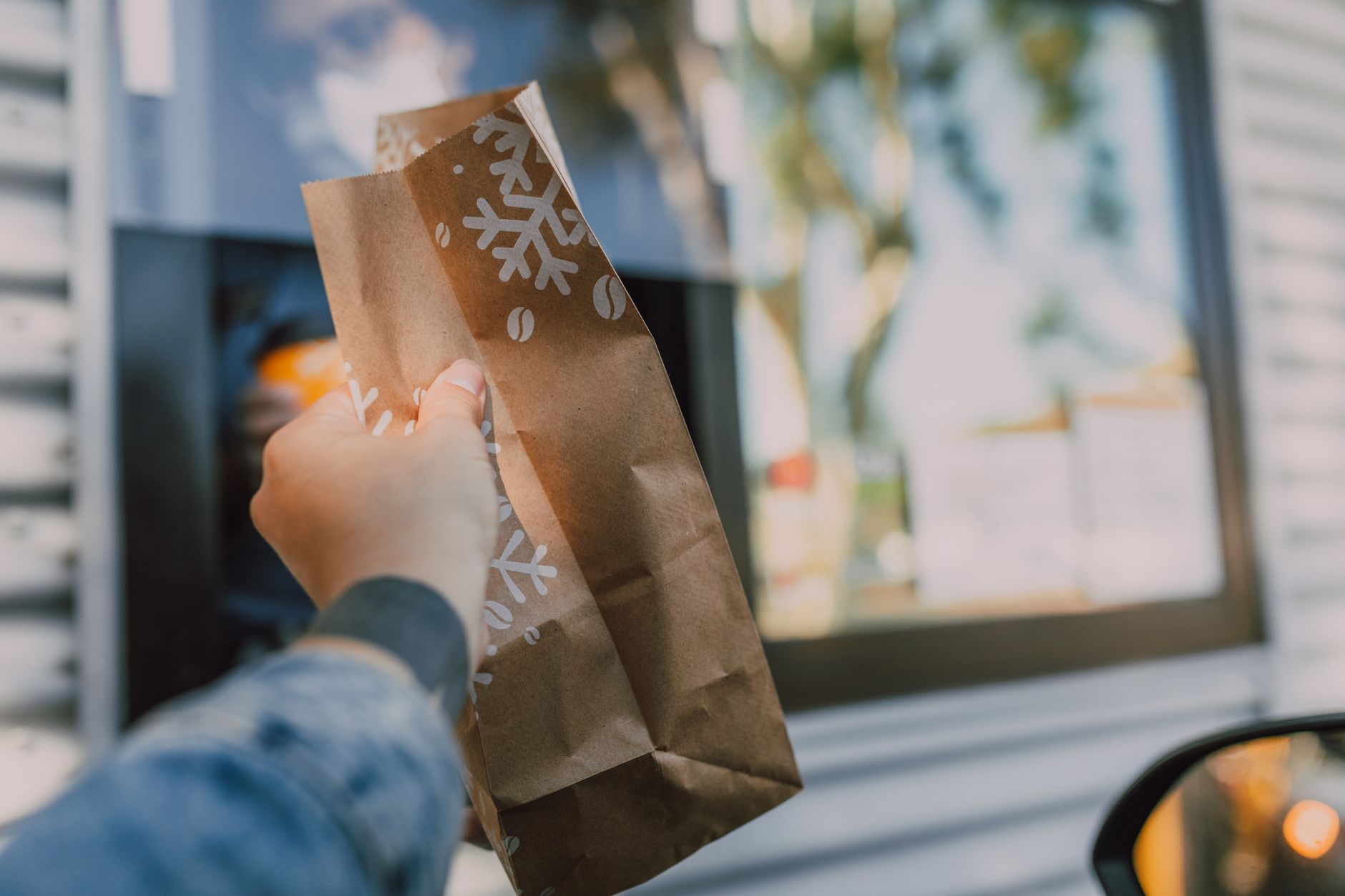 A restaurant employee hands a prepared order to a customer waiting outside the drive-through.