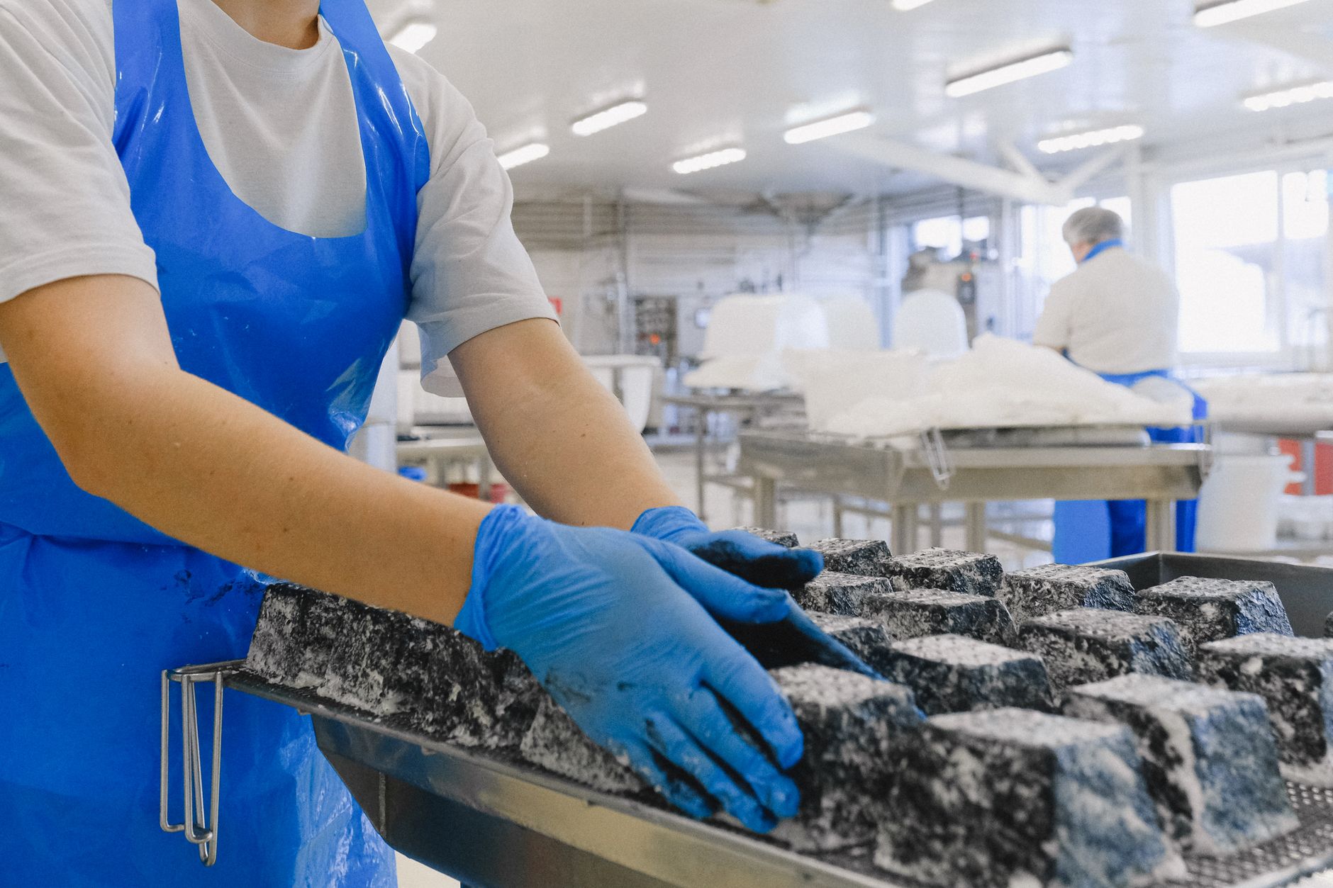 A worker in protective clothing handles food on a live production floor, reflecting the staffing and changeover pressures on a frozen-meal line.