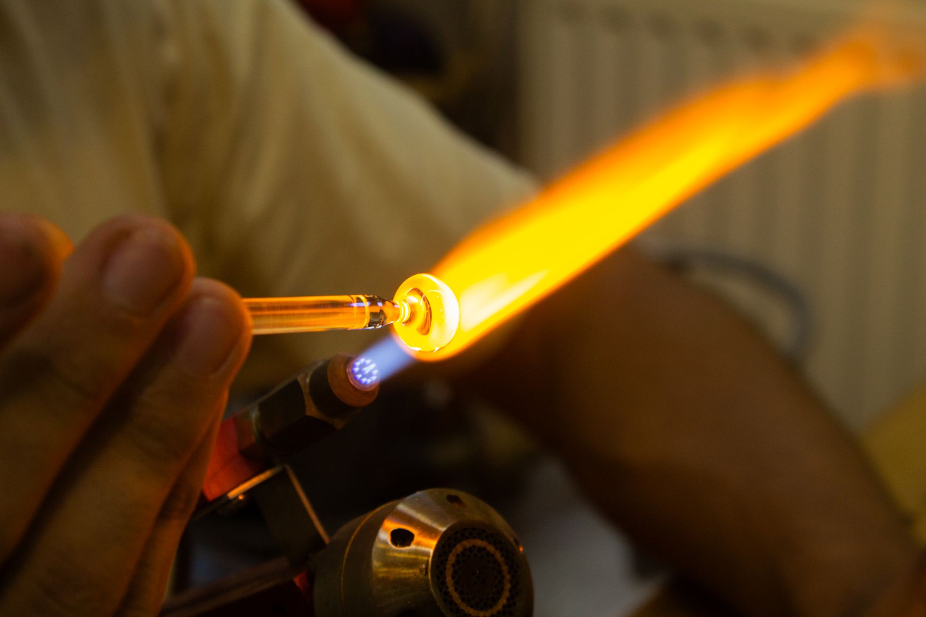 Glass tubing being carefully heated and formed over a torch flame in a workshop.