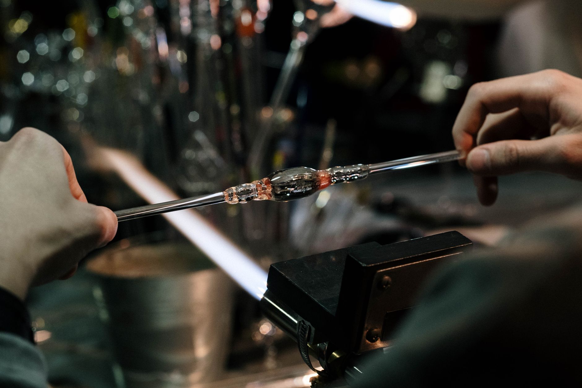 A skilled glassworker shaping laboratory glass tubing with a flame in a specialty workshop.