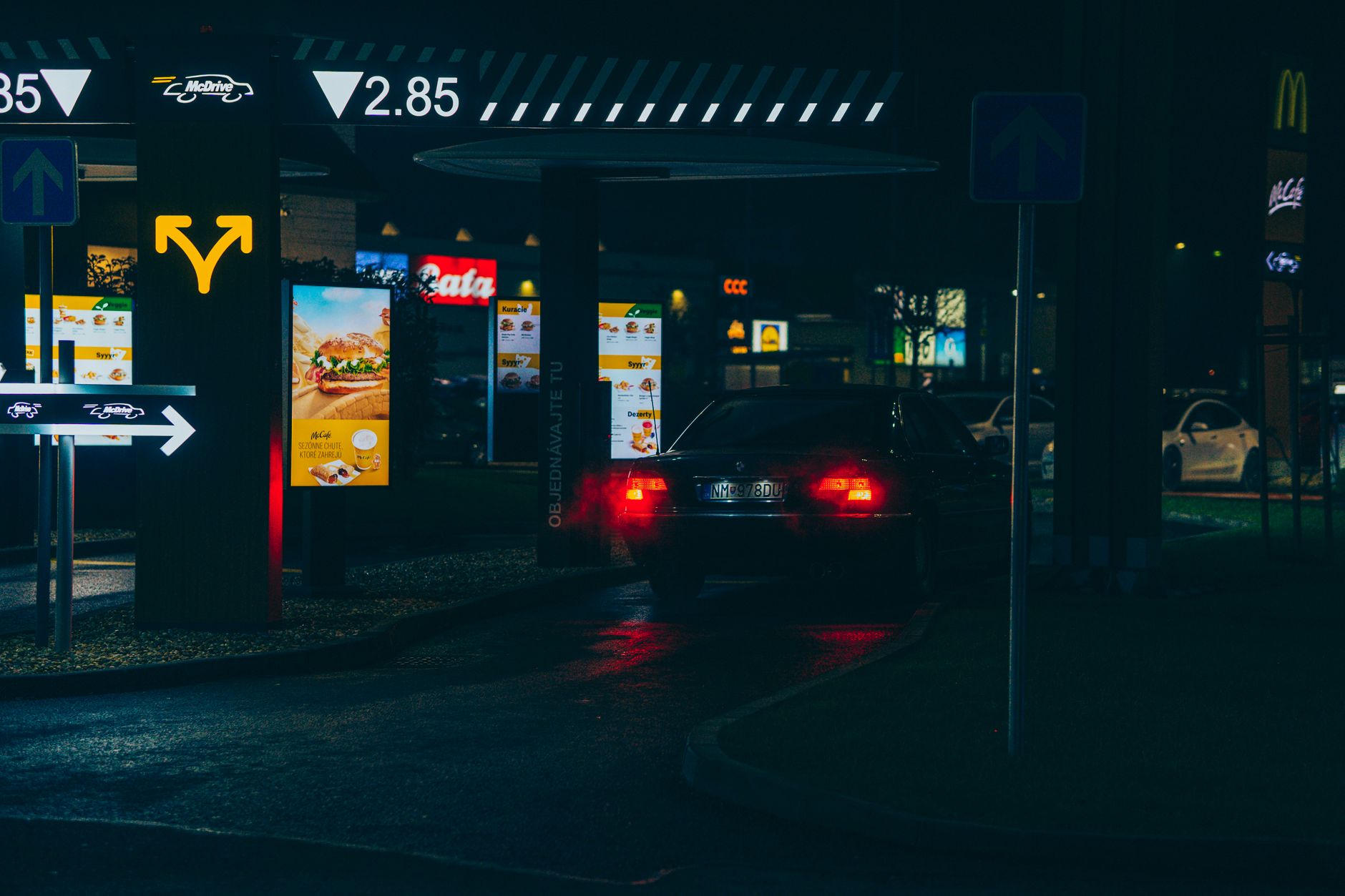 A quick-service restaurant at night with drive-thru lanes lit up while delivery orders still move inside.