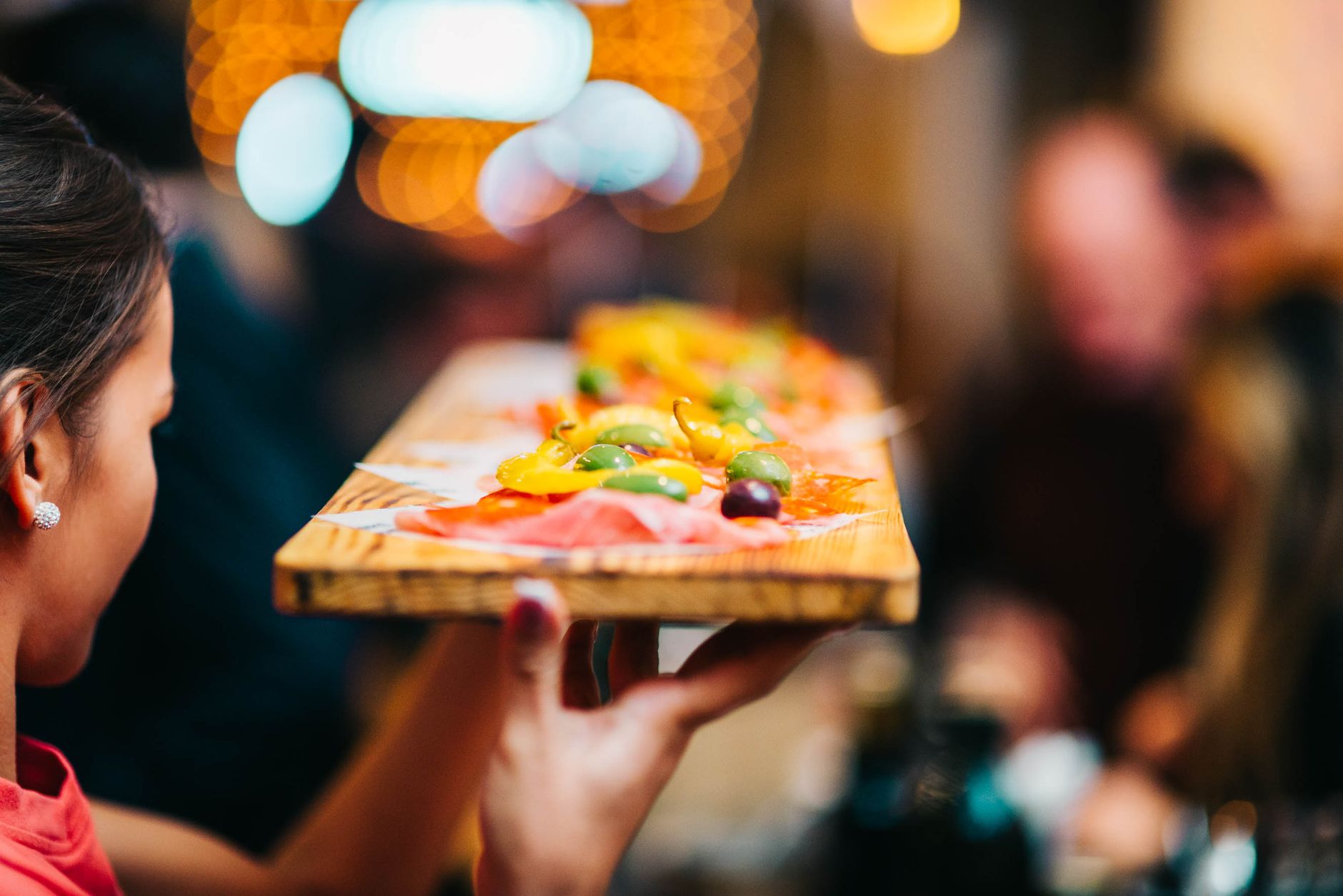 A restaurant server carries prepared dishes through the dining room during service.