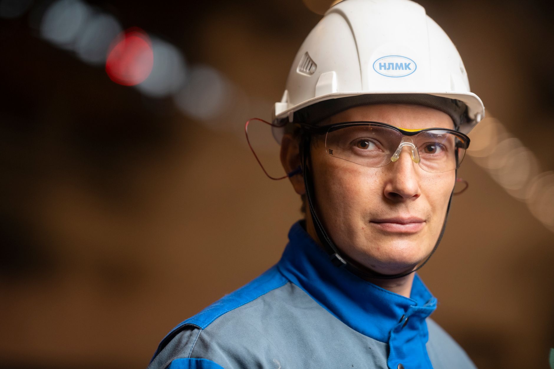 Technician in protective gear standing on a plant floor near wet equipment.