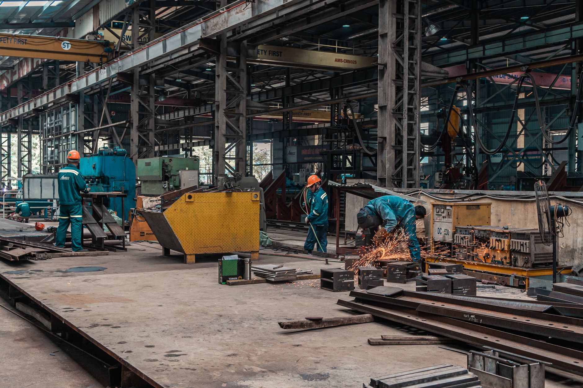 Two fabrication workers position steel components together on a busy workshop floor.