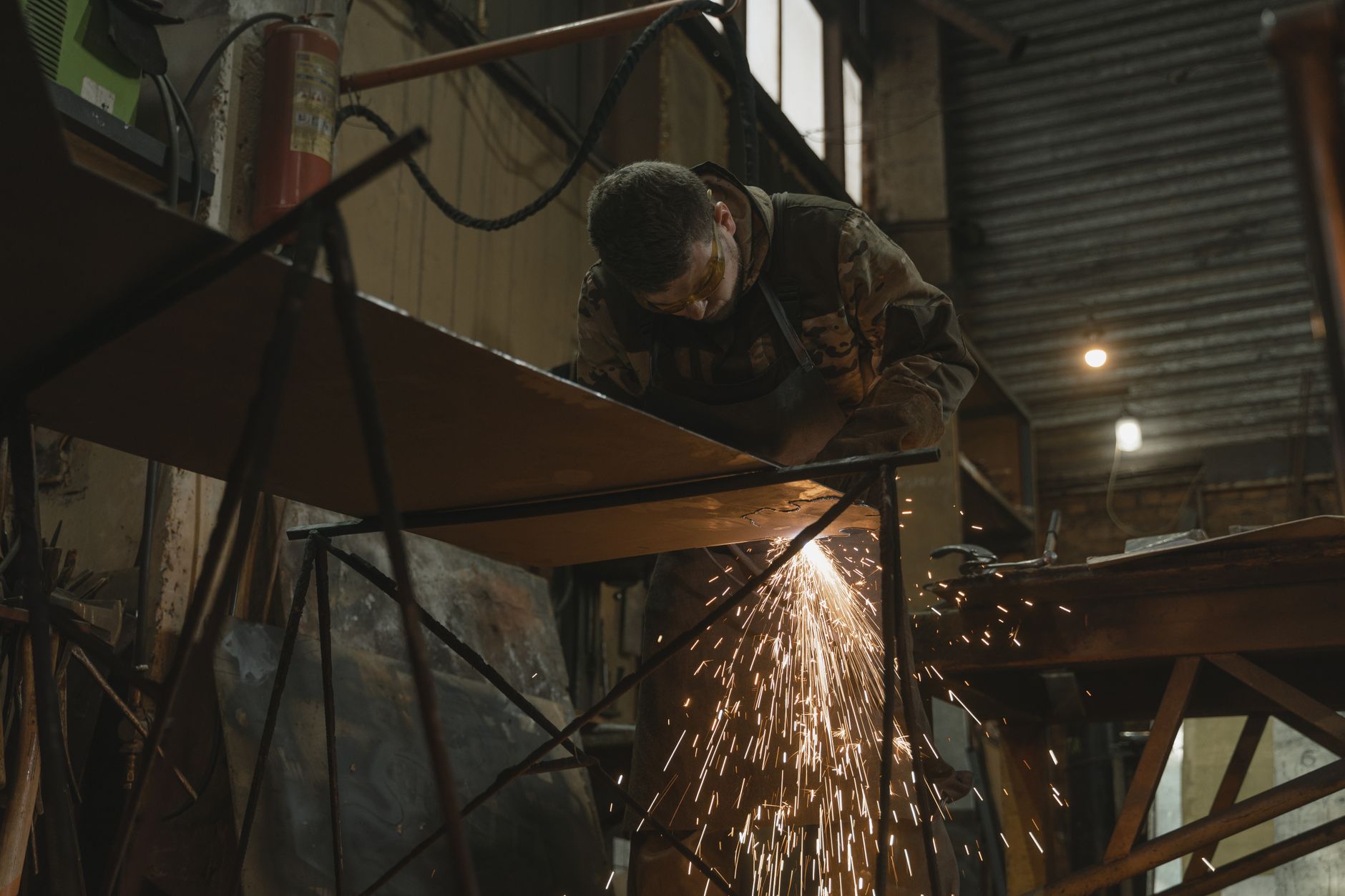 Sparks fly as a welder finishes a steel frame in a fabrication shop.