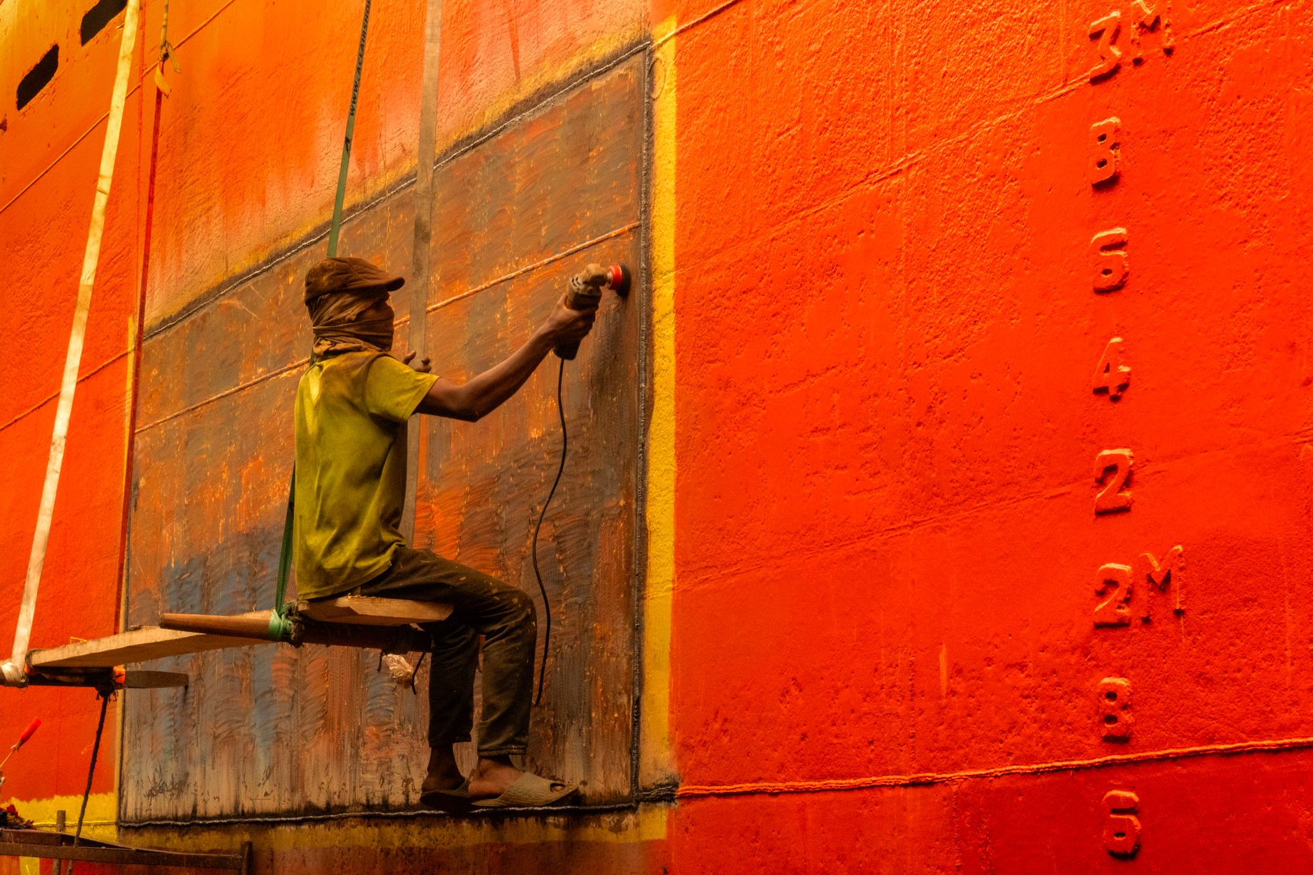 A metalworker sands a fabricated steel part in a busy finishing workshop.