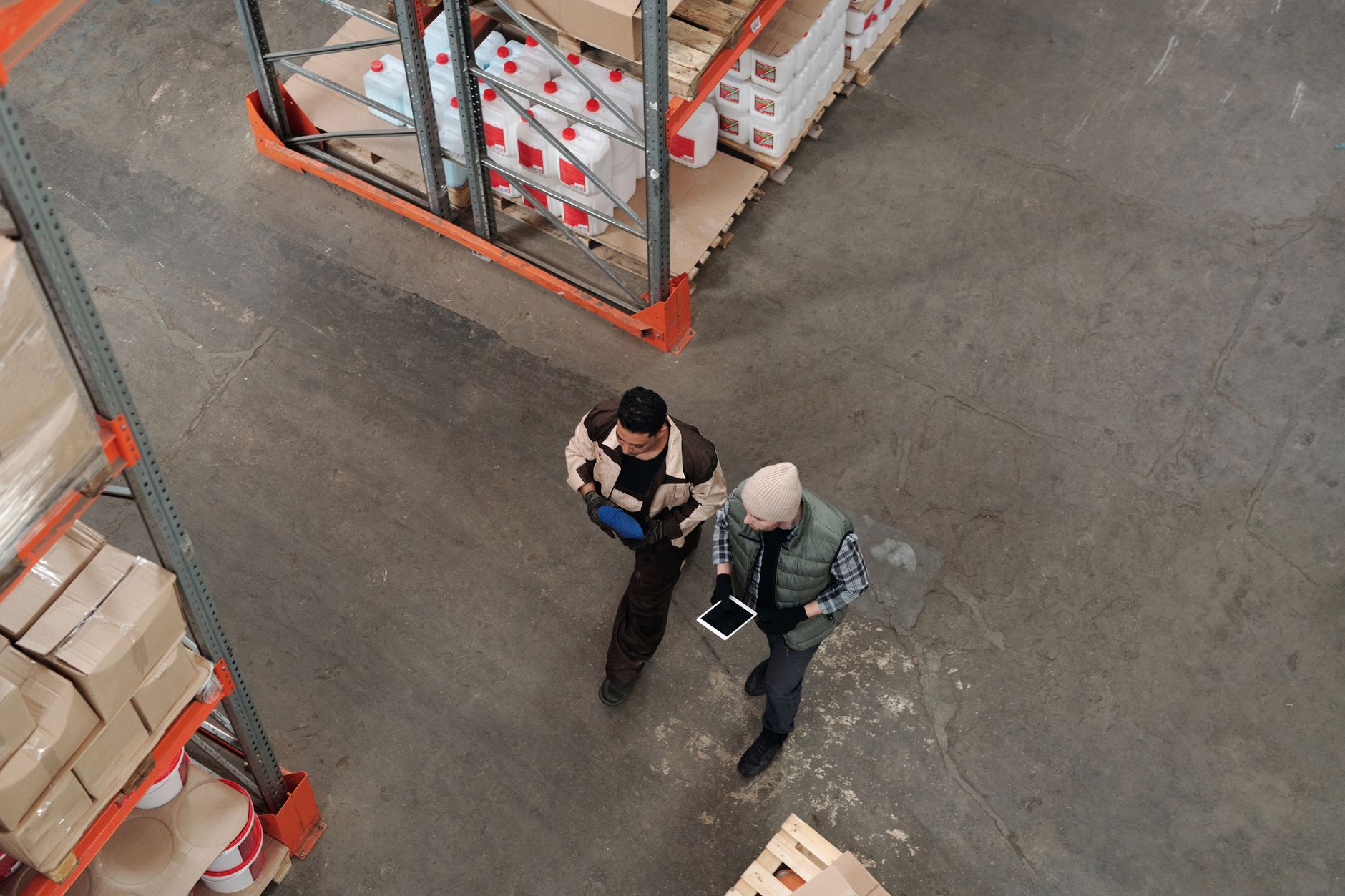 Manufacturing staff review operational data on a tablet beside an active warehouse aisle.