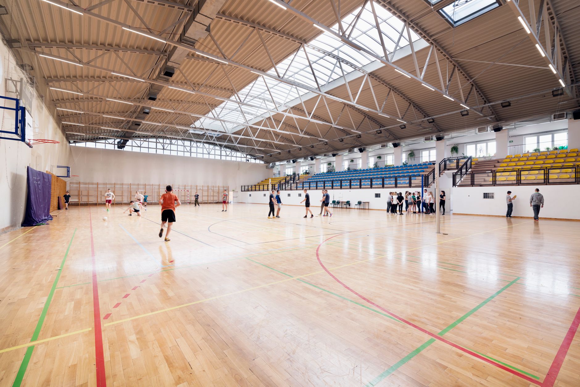 Wide view of an indoor community basketball gym with polished hardwood floors under bright overhead lights.