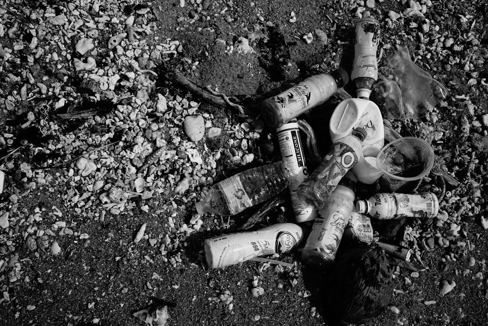 Discarded plastic bottles and foam scattered along a rocky shoreline near the waterline.