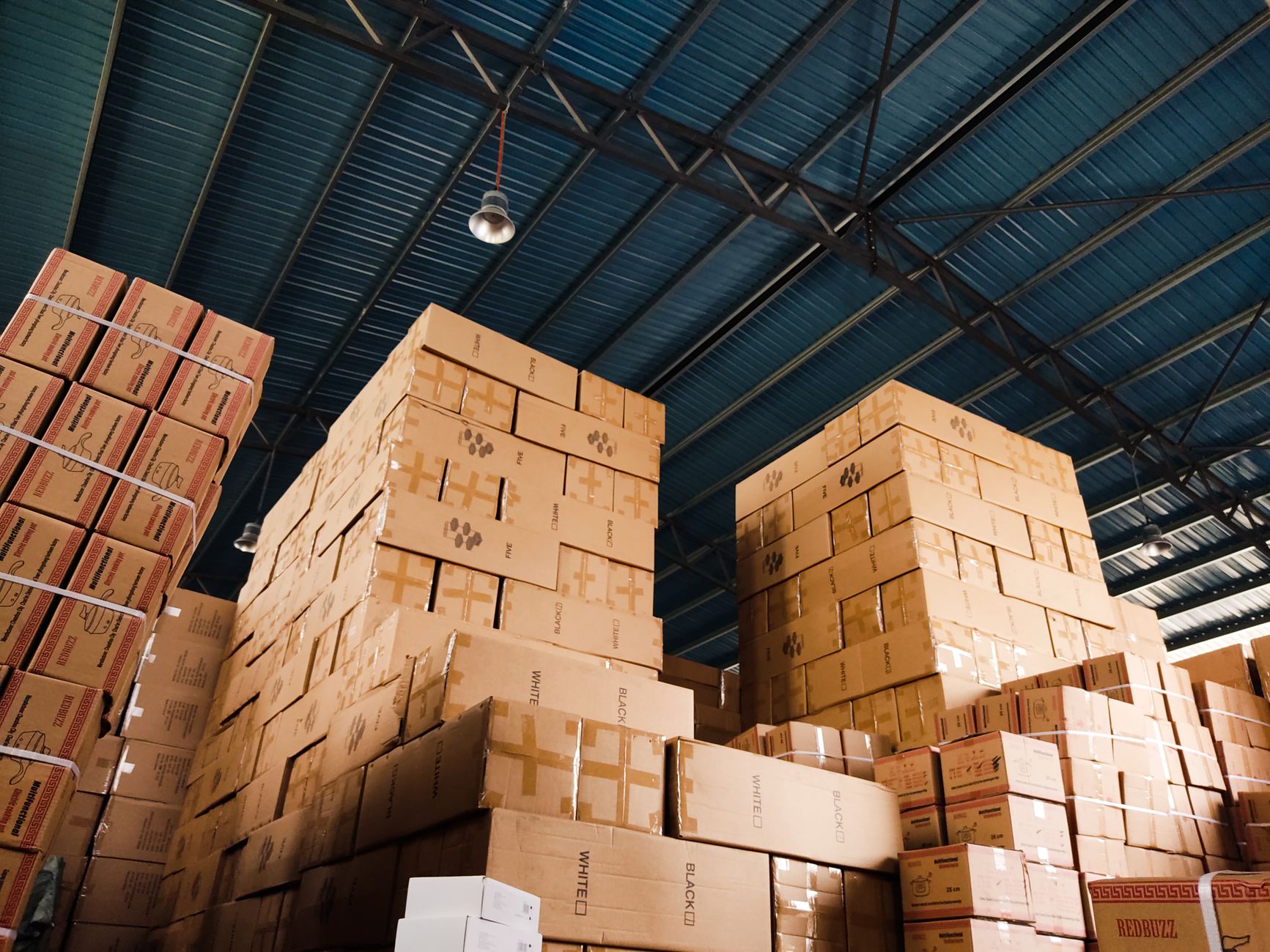 Stacks of sealed cardboard cartons on pallets in a clean packaging area, setting the scene for a labor-intensive glove packing line.