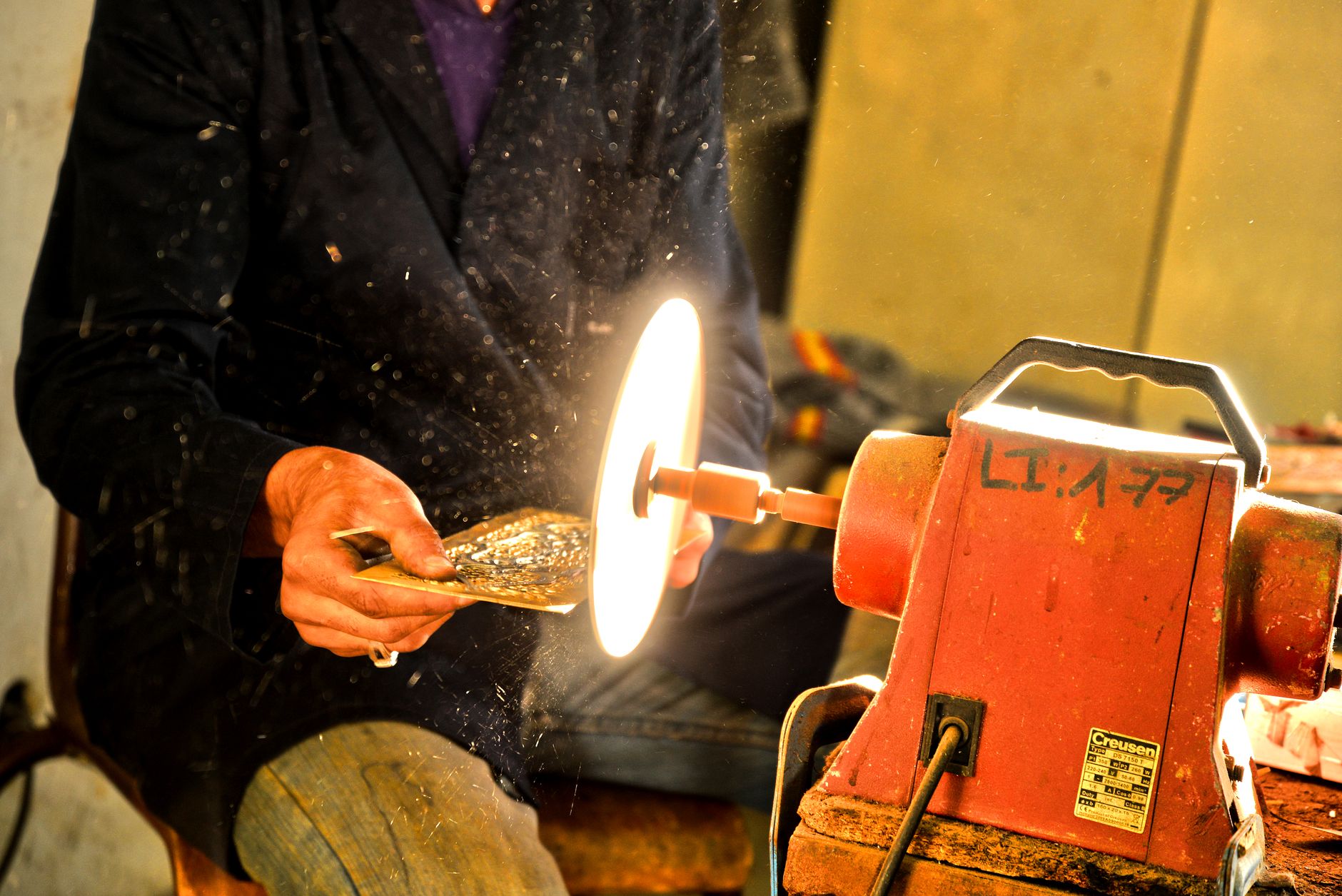 A worker hand-polishes a metal part, illustrating the repetitive finishing work transferred to the compact cell.