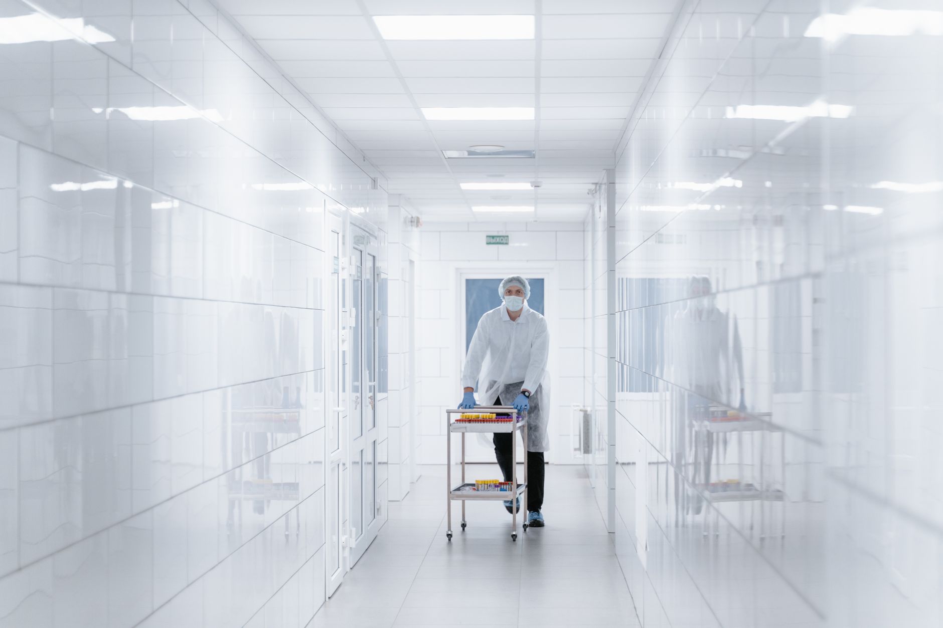 Workers in protective gowns walk through a sterile-looking manufacturing hallway.