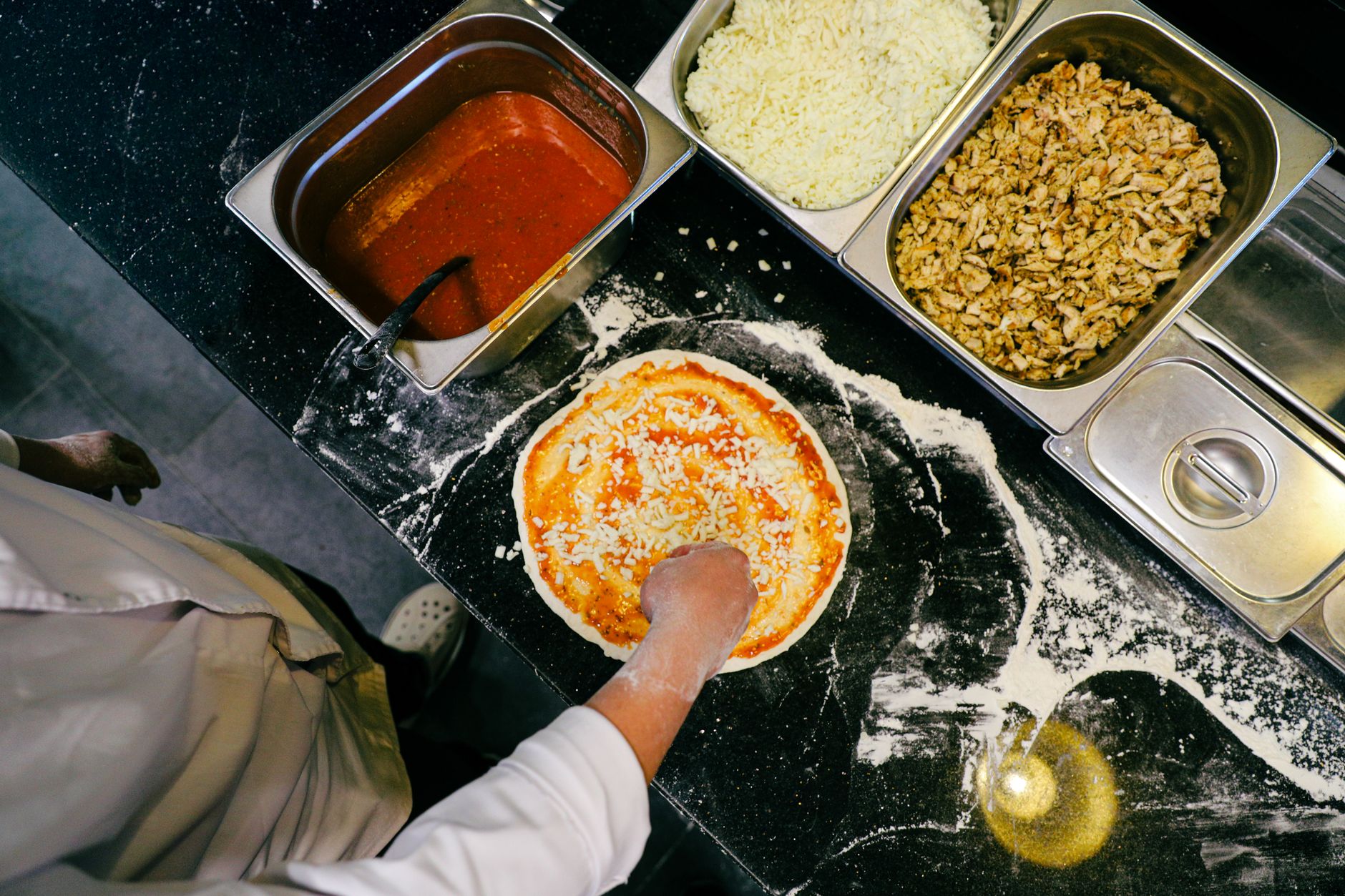 Portioned pizza toppings and ingredients are arranged at a commercial kitchen prep station.