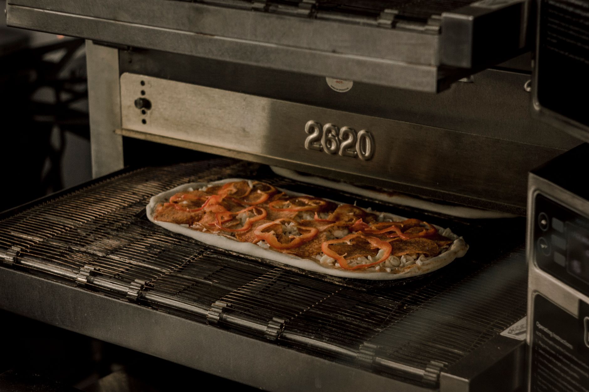 Fresh pizzas move through the oven area of a high-volume pizzeria kitchen.