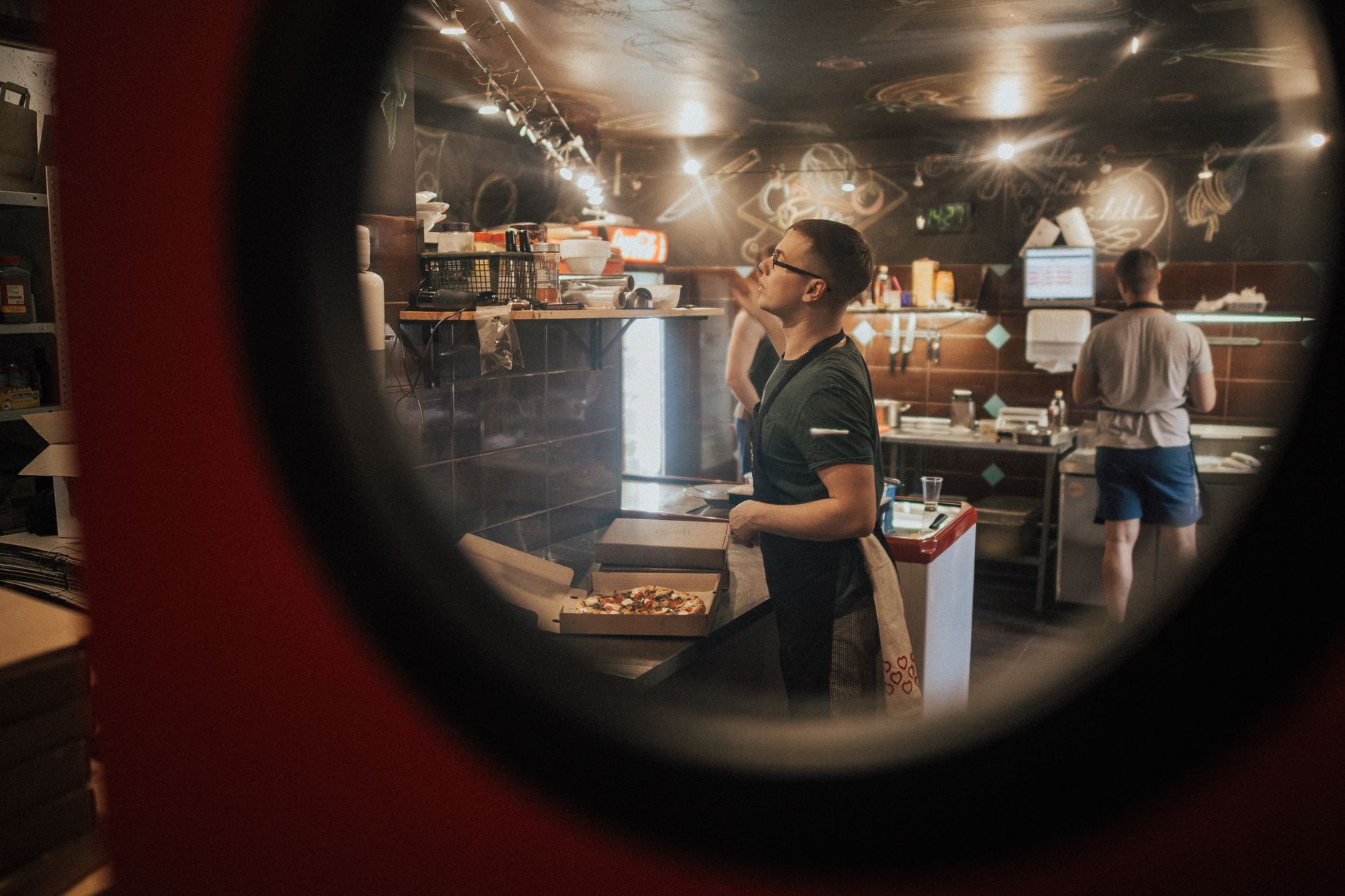 Pizza makers assemble orders during a busy shift in a commercial pizzeria kitchen.