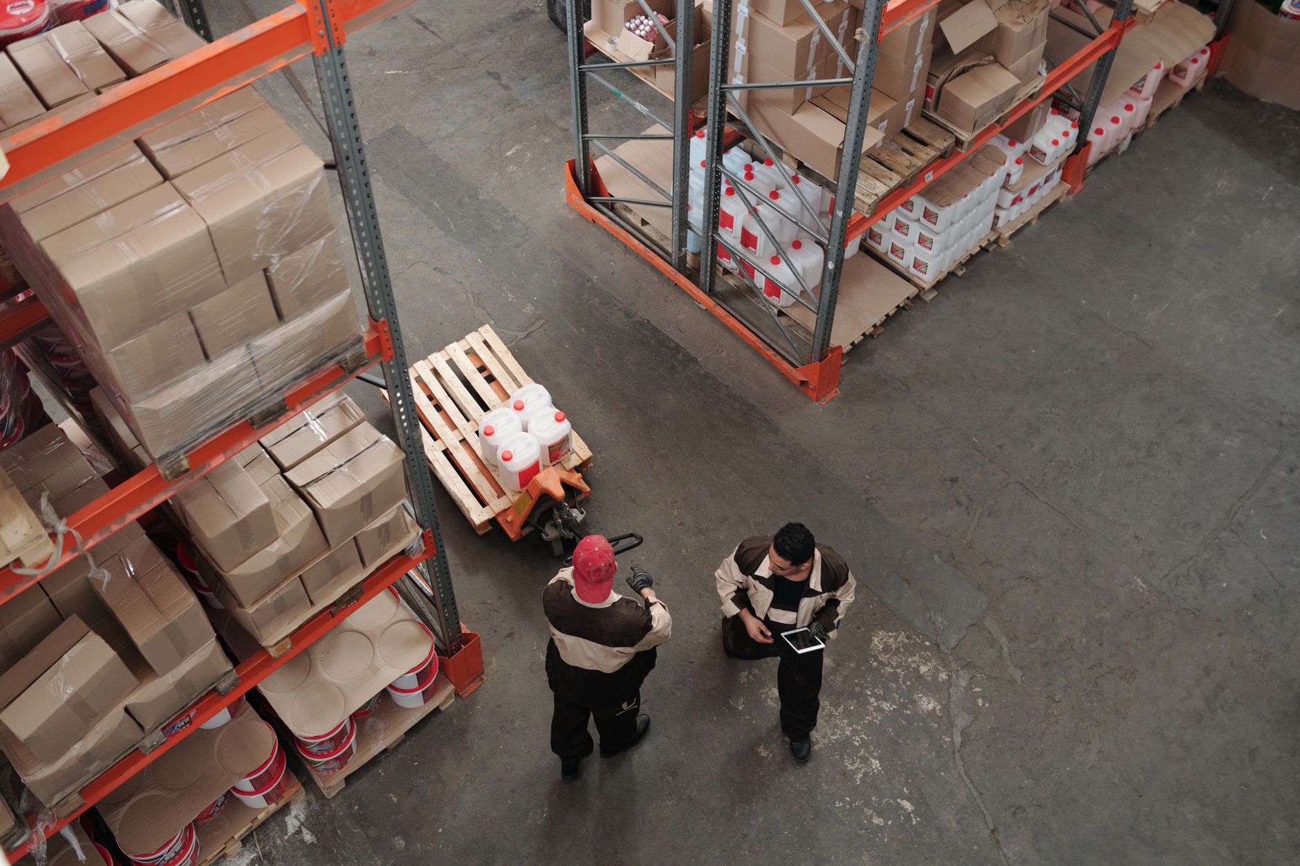 Workers move materials through a spacious automotive-components plant warehouse.