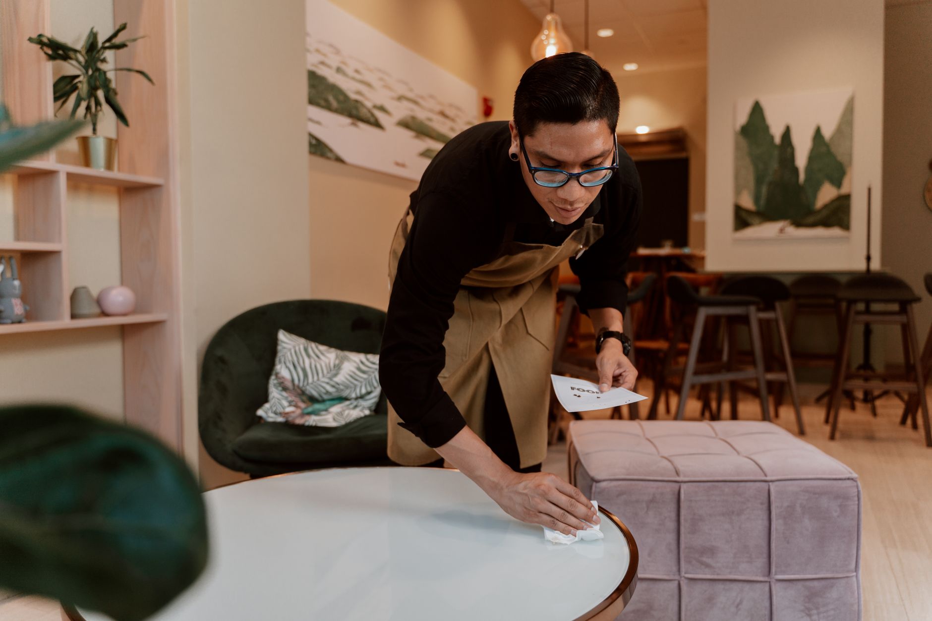 A worker wiping down tables in a public library reading area.