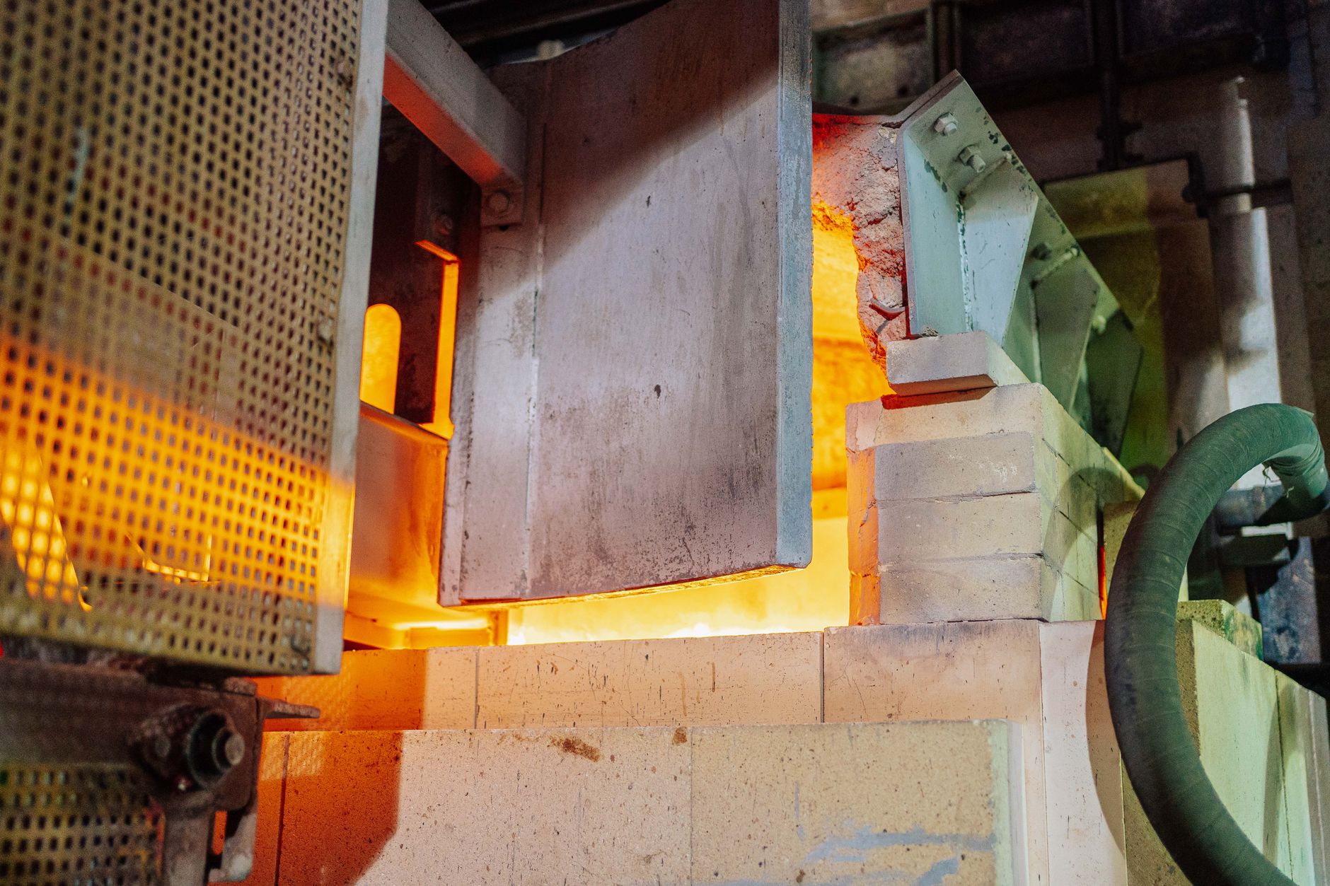 A glowing industrial furnace illuminates the hot-work area of a glass products factory.