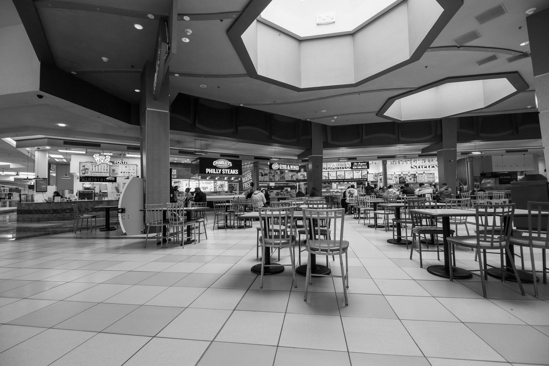 Visitors gather in a busy mall food court with wide open flooring.