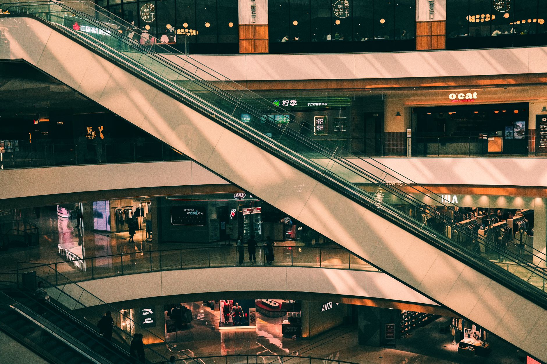 Shoppers walk through a bright indoor mall concourse with polished tile floors.