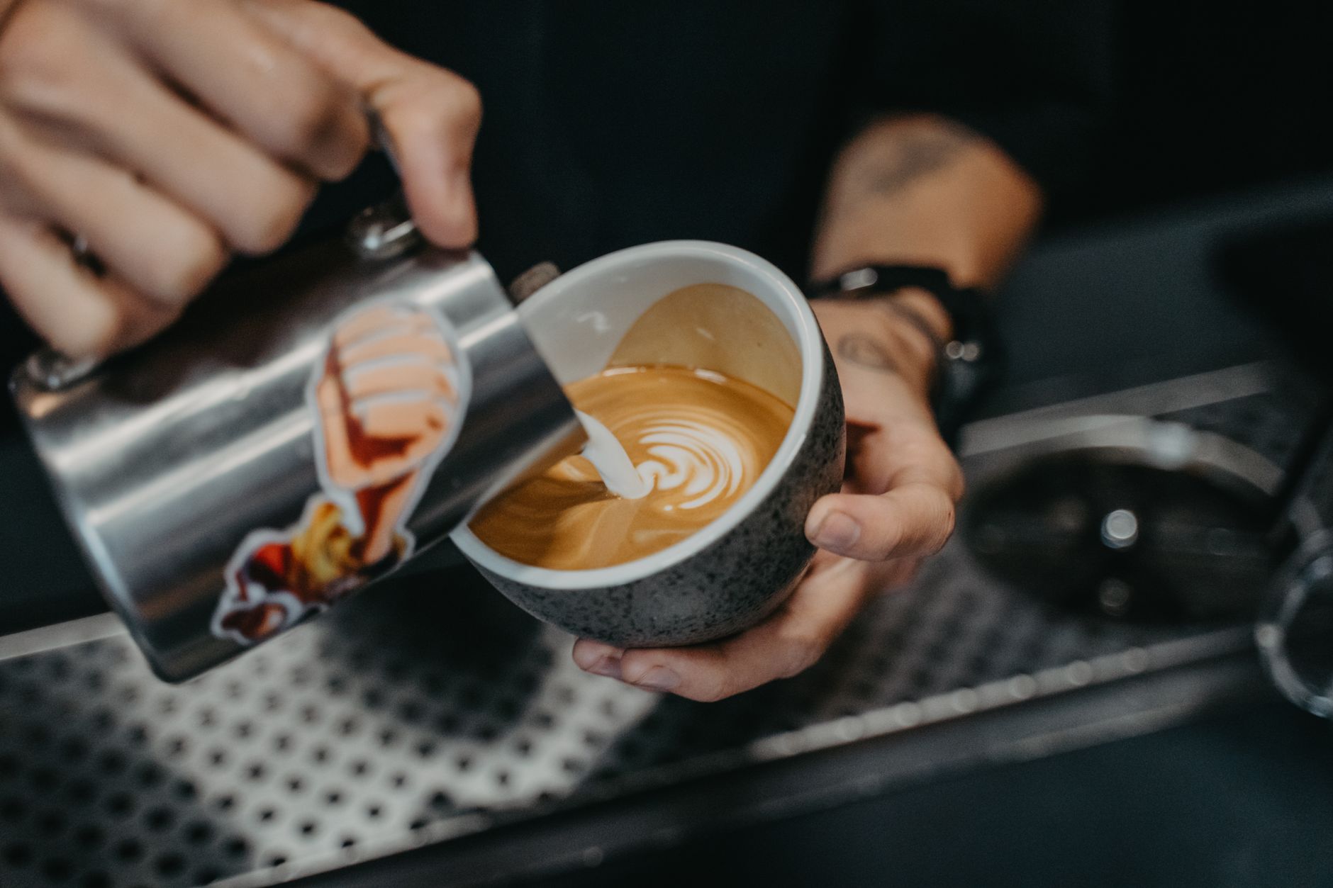 A barista carefully pours a drink behind a working cafe counter.