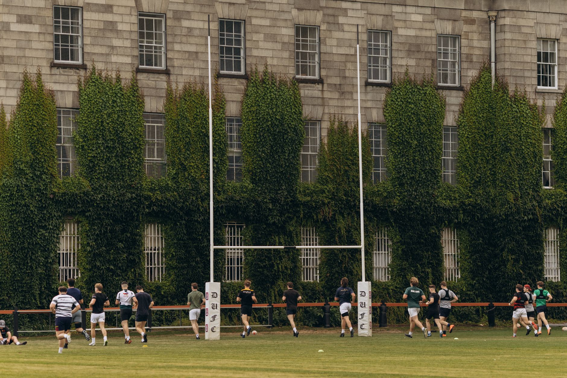 Players training on a natural-grass rugby pitch, reflecting how mowing schedules had to fit around evening field use.