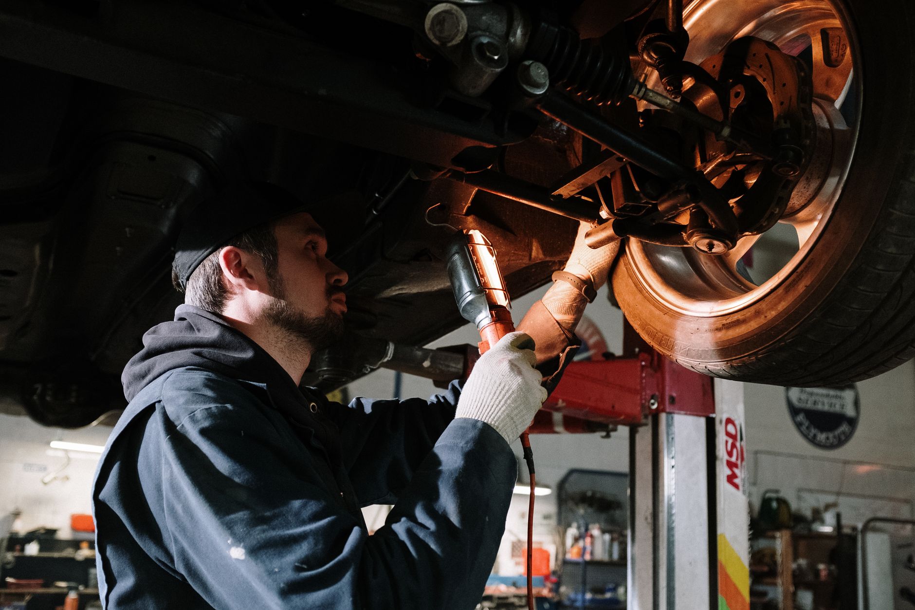 An automotive technician concentrates on repair work beneath a vehicle raised on a service lift.