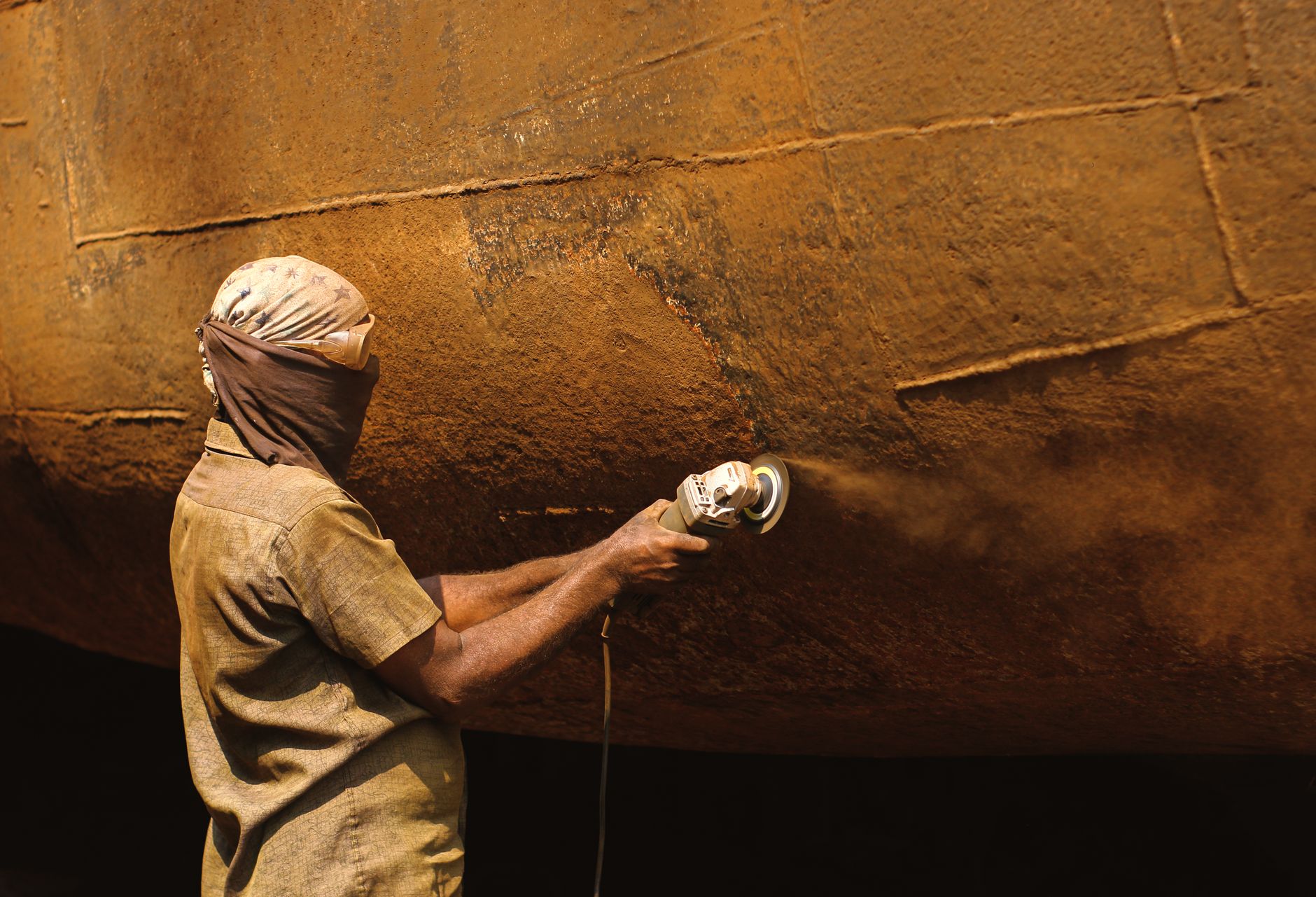 Protective blasting gear illustrates the severe working conditions involved in preparing steel hulls.