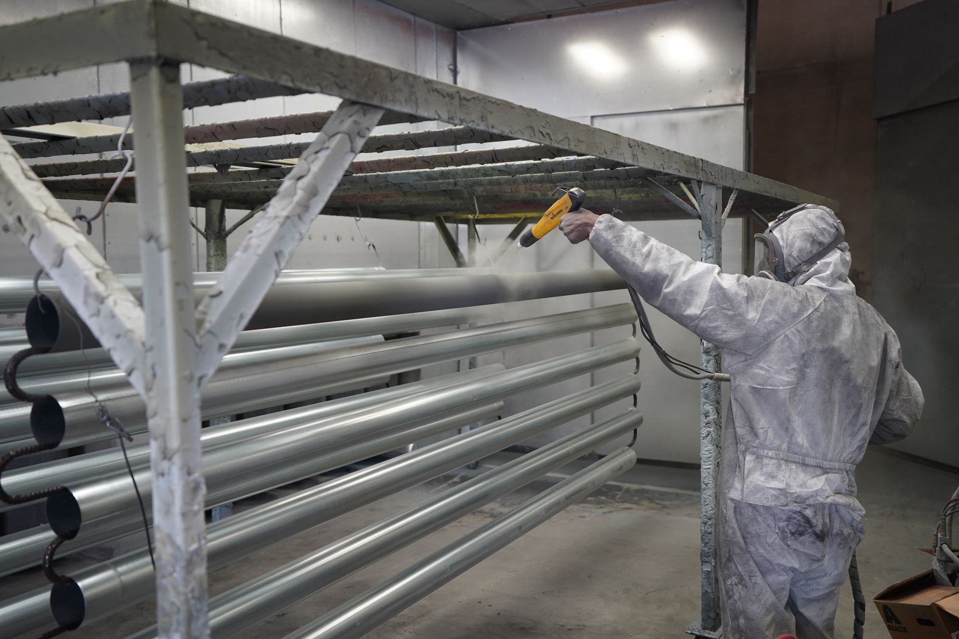 A protected worker performs abrasive blasting inside a large shipyard work area.