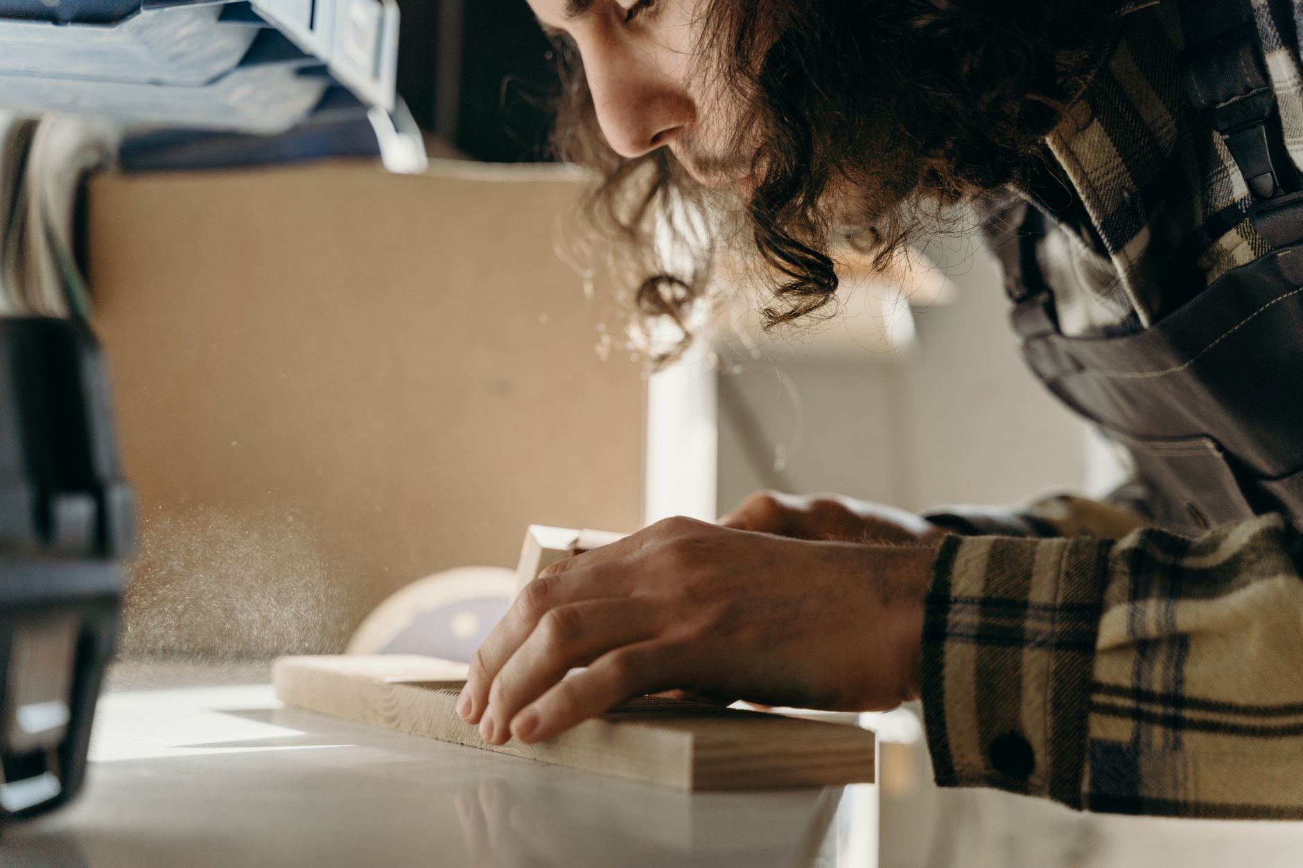 Close view of hands smoothing a wood surface on a workbench with dust in the air.