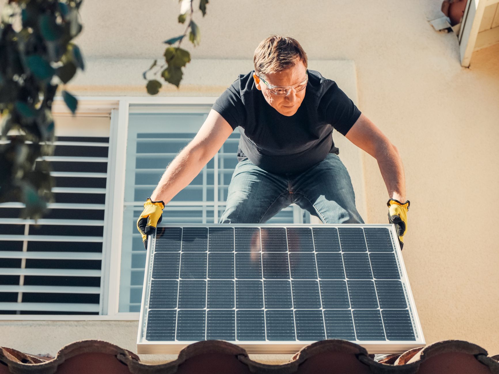 Workers install mounting components beneath rows of solar panels at a large outdoor site.