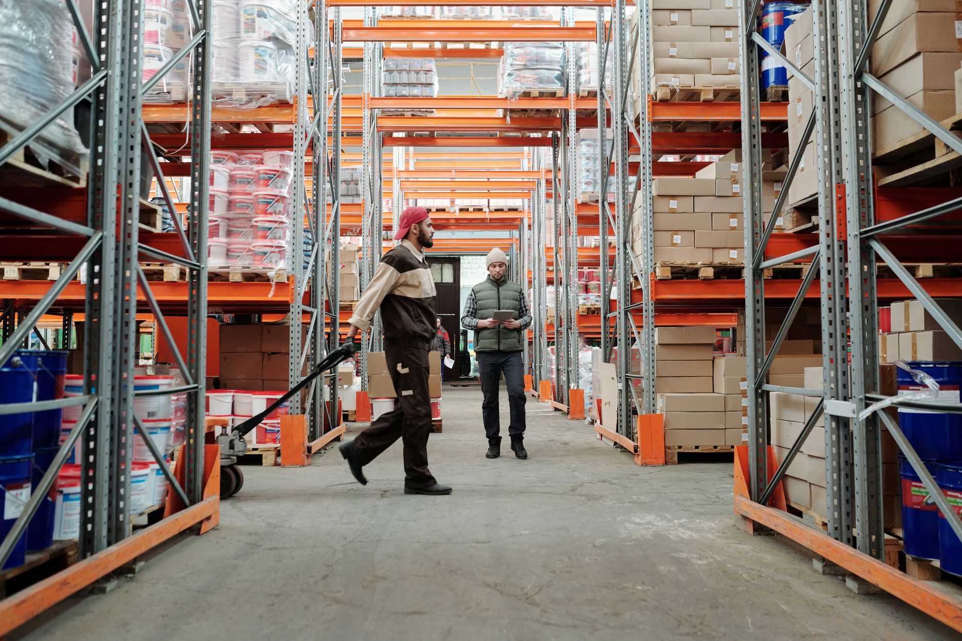 A worker walks a long pick path between tall shelving in a distribution center.