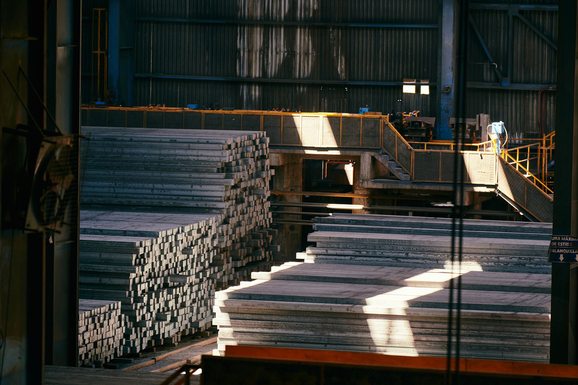 Workers handle metal components inside a confined industrial surface-finishing plant.