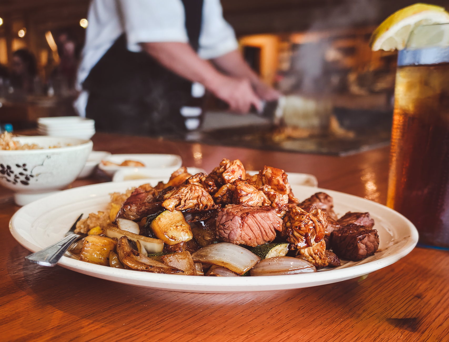 A chef prepares food on a teppanyaki grill in a busy full-service restaurant.
