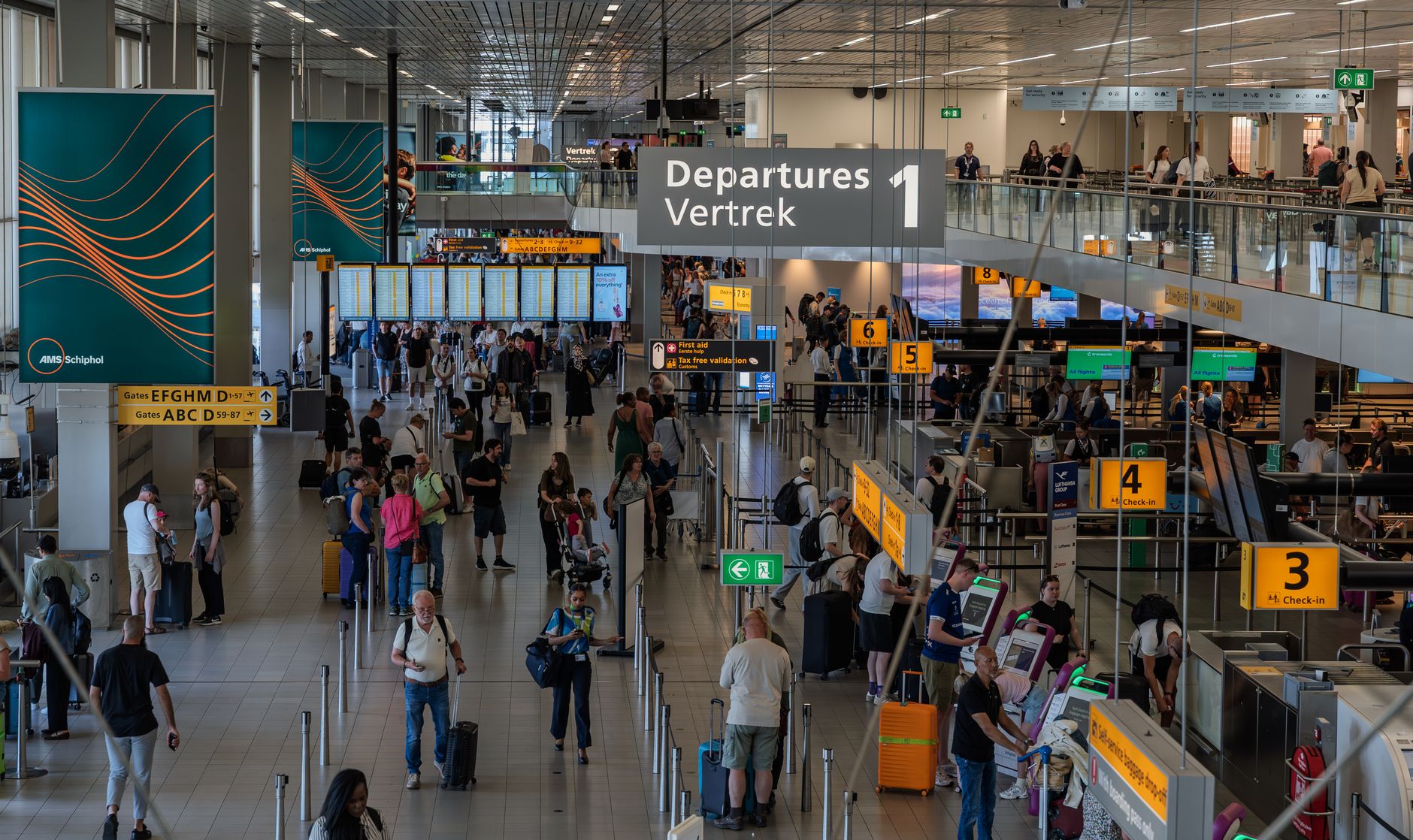 Travelers move through a busy international airport departure hall beneath check-in and flight information displays.